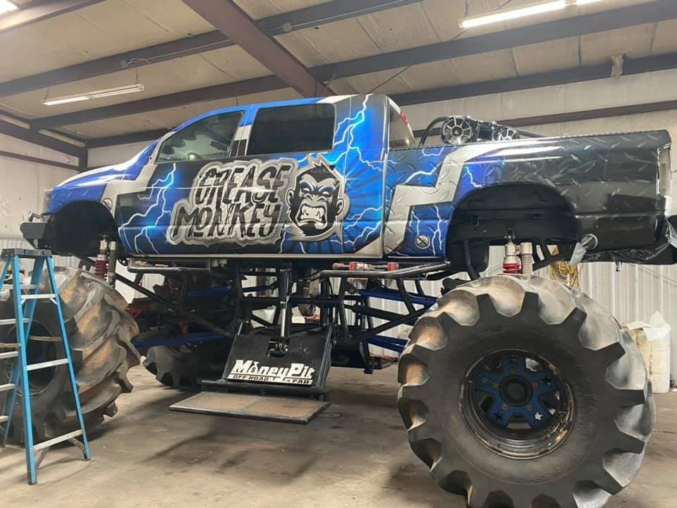 Monster truck with a blue and black design and the logo 'Beast Mokes' on the side, inside a garage or workshop.