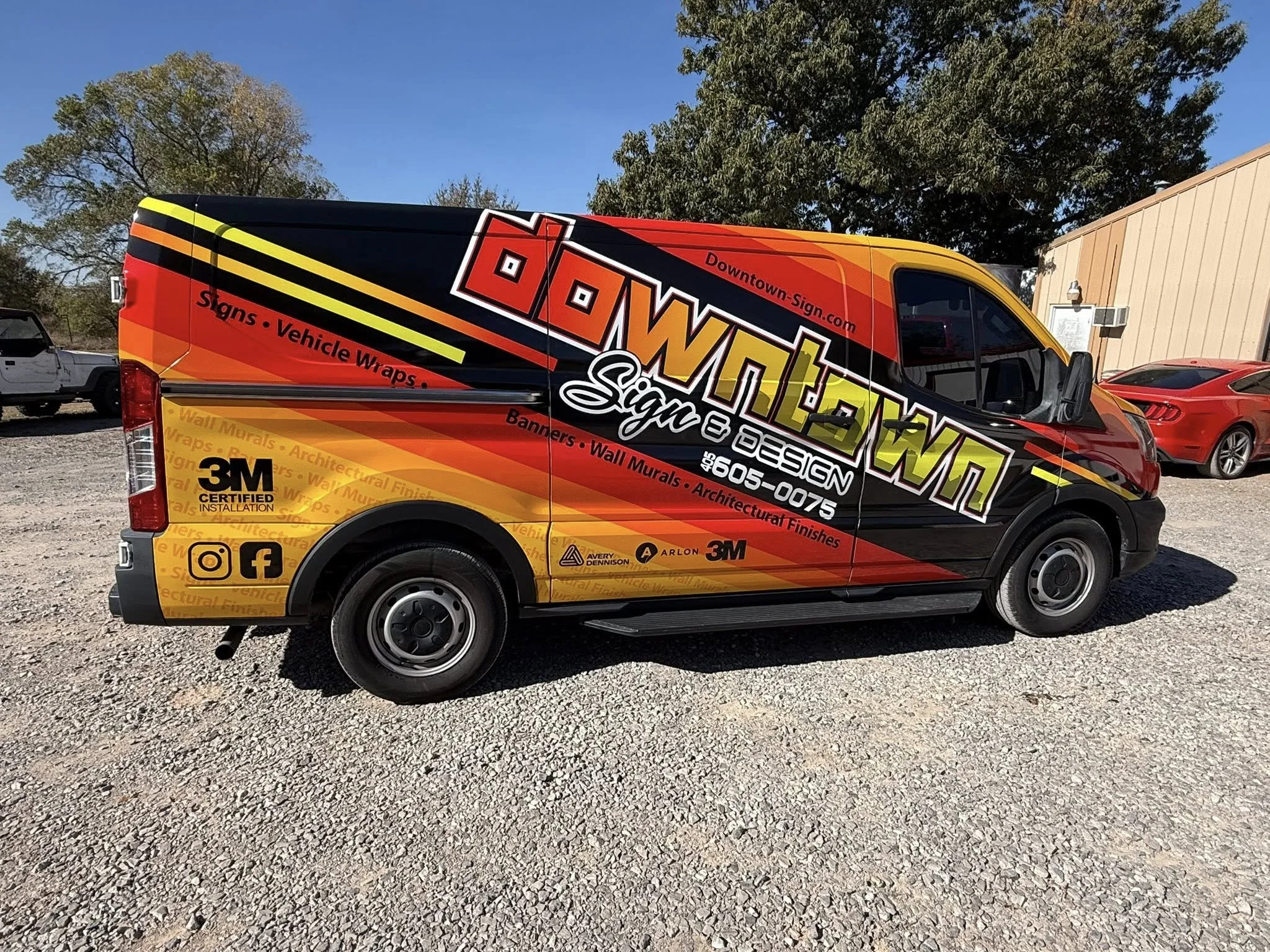 A promotional vehicle wrap for Downtown Sign on a commercial van, featuring a red, orange, black, and yellow design with contact information, social media icons, and services like signage, vehicle wraps, banners, and architectural finishes.