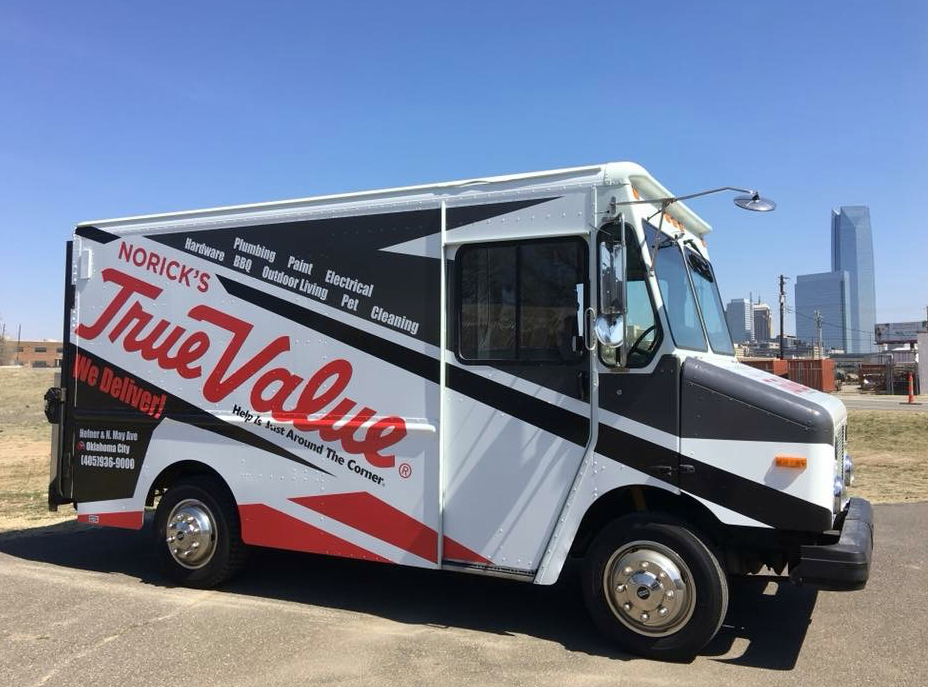 Delivery van with Norick's True Value logo and services listed, parked outdoors with a city skyline in the background.