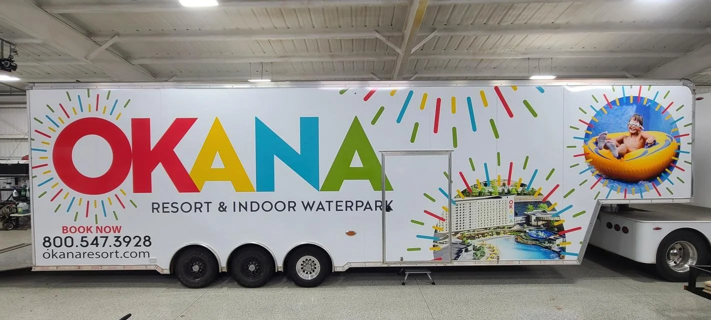 A large promotional trailer for OKANA Resort & Indoor Waterpark with colorful design, featuring a child sliding in a yellow inner tube and a waterpark image with slides and a lazy river.