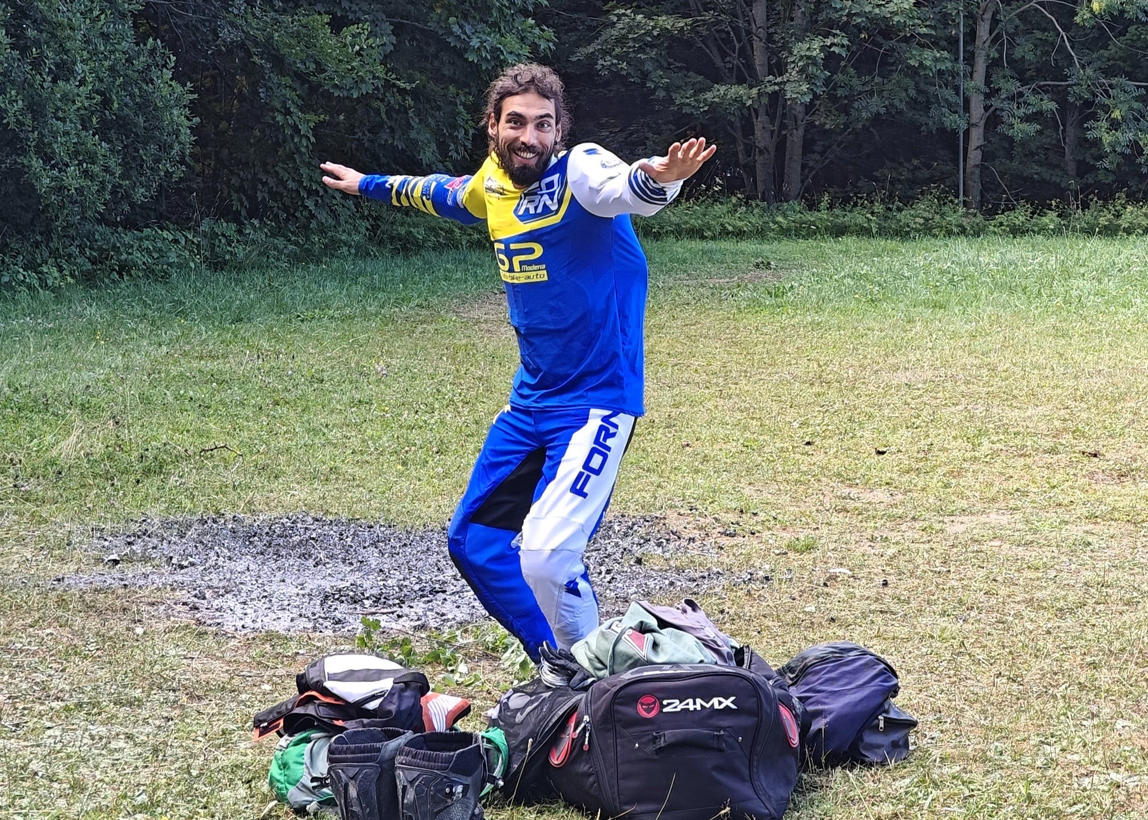 Uomo in abbigliamento da moto sul prato con bagagli, che sorride con le braccia aperte