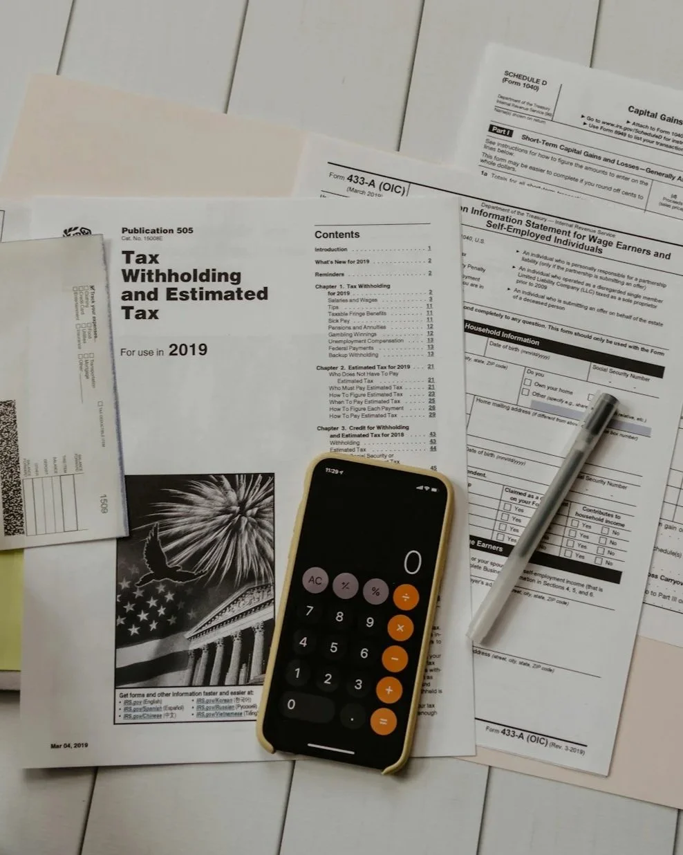 Tax documents, a calculator, and a pen on a white wooden surface.