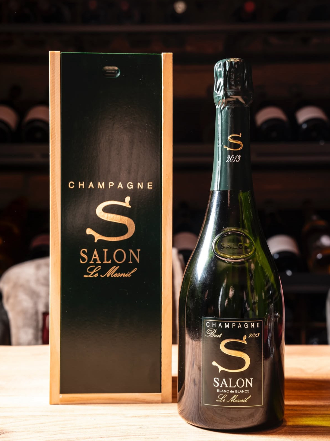 Bottiglia di champagne e scatola regalo, entrambi con etichetta nera con scritte dorate e un grande s simbolo, a tema 2013, in un negozio di vini.