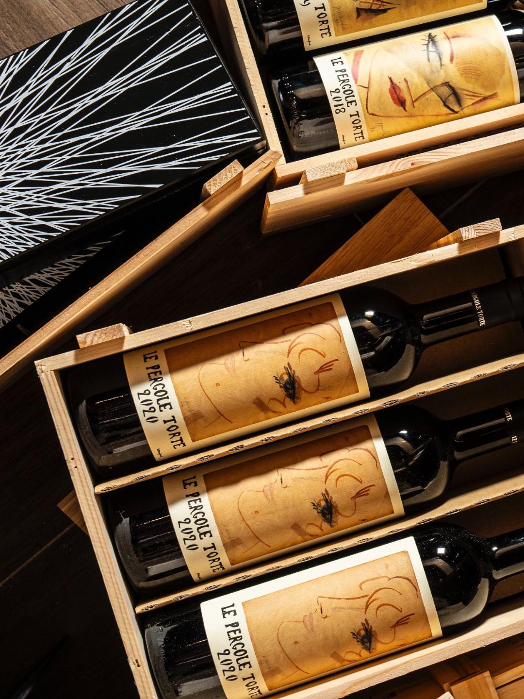 Sei bottiglie di vino in cassette di legno, etichettate con il nome 'Le Percole Torte 2018' e con un disegno artistico di un volto femminile.