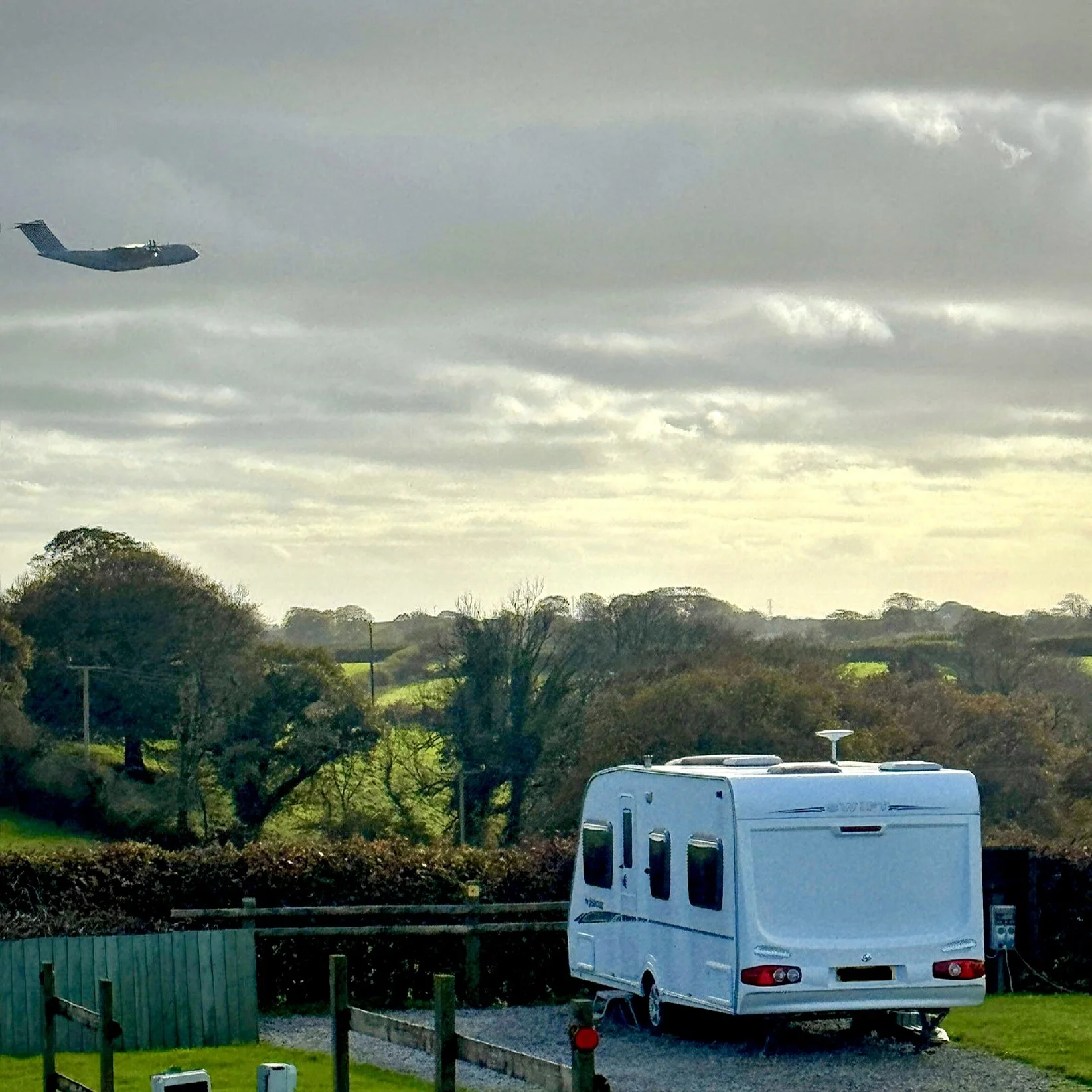 a caravan parked on a hard stand pitch looking down the valley while a plane does a low pass overhead 
