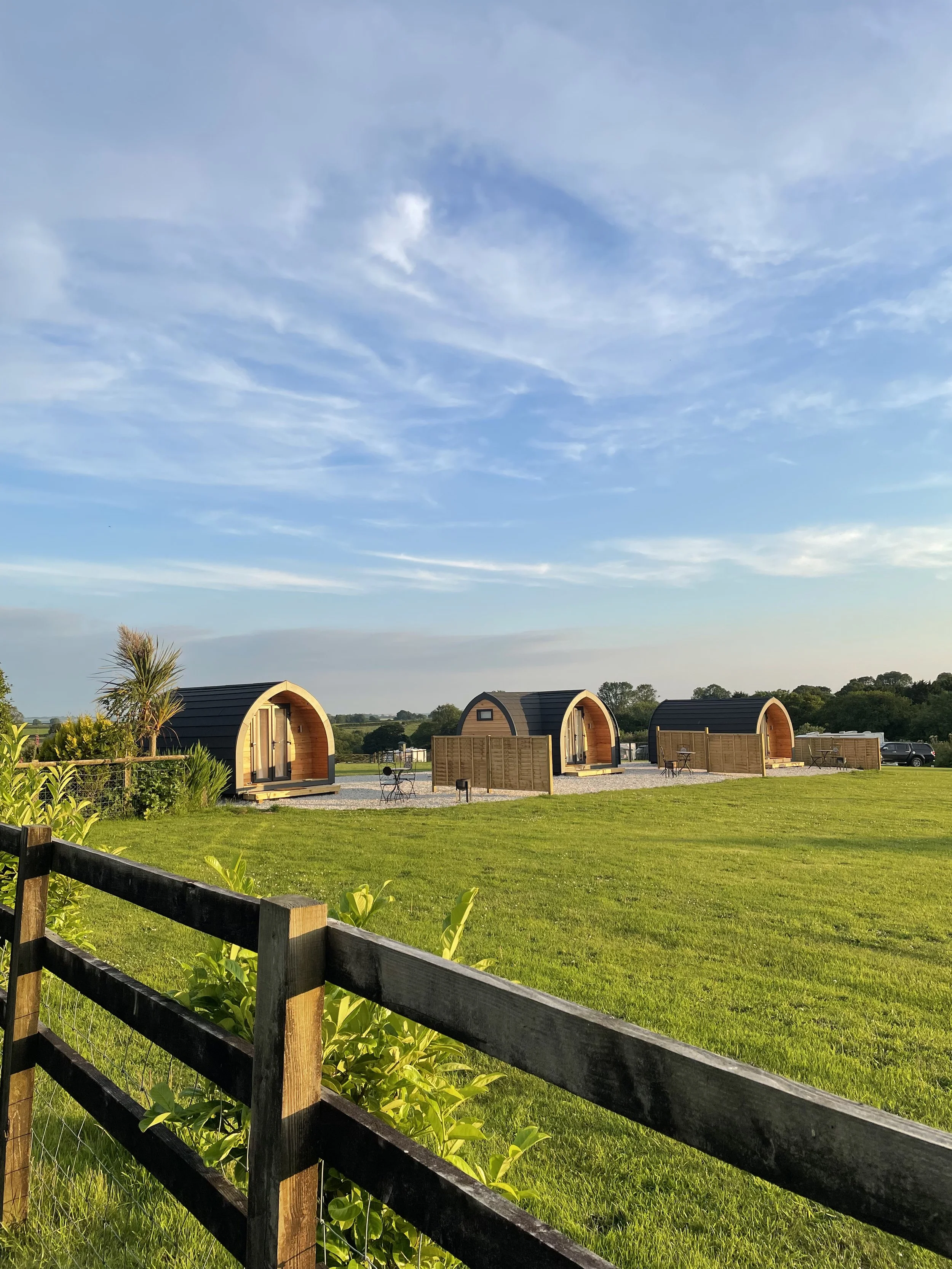 Three cosy glamping pods looking out to the summer evening sunset, with views up onto Caradon moor in the luscious Cornish countryside