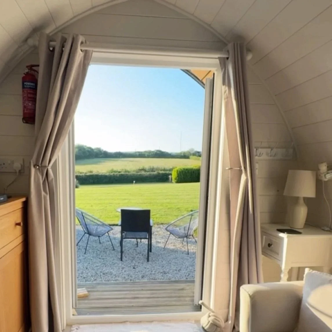 Open door leading to a patio with chairs and a green field beyond.