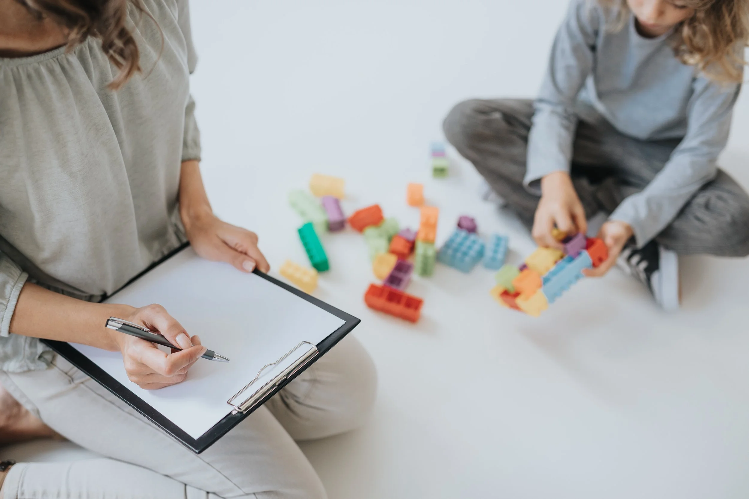 Deux enfants jouent avec des blocs de couleur, un enfant prend des notes sur un tableau blanc.