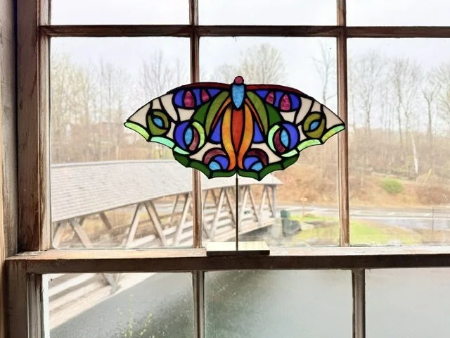 Colorful stained glass butterfly lamp on a windowsill with a view of trees and a building outside.