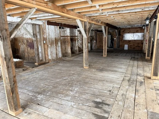 Interior of an unfinished wooden structure with exposed beams, support posts, and a weathered wooden floor.