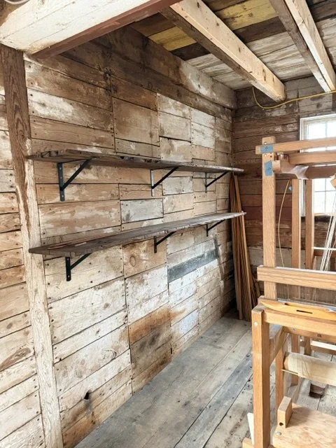 A rustic wooden room with two wall-mounted shelves and wooden furniture.