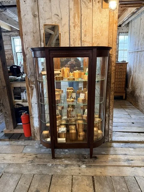 A glass display cabinet filled with wooden objects, placed on a rustic wooden floor inside a wooden building.