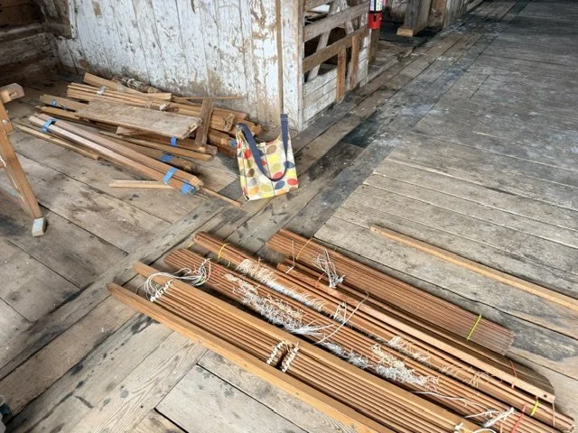 Bundles of wooden slats and laths on a rustic wooden floor in a workshop or storage area.