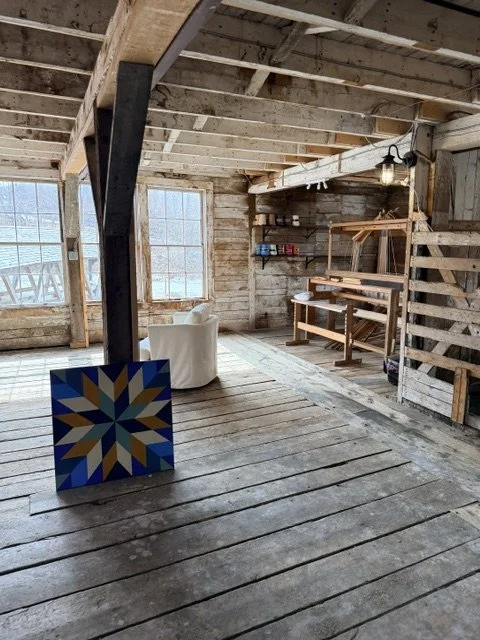 Interior of an unfinished wooden building with large windows, a white armchair, and a wooden workbench.
