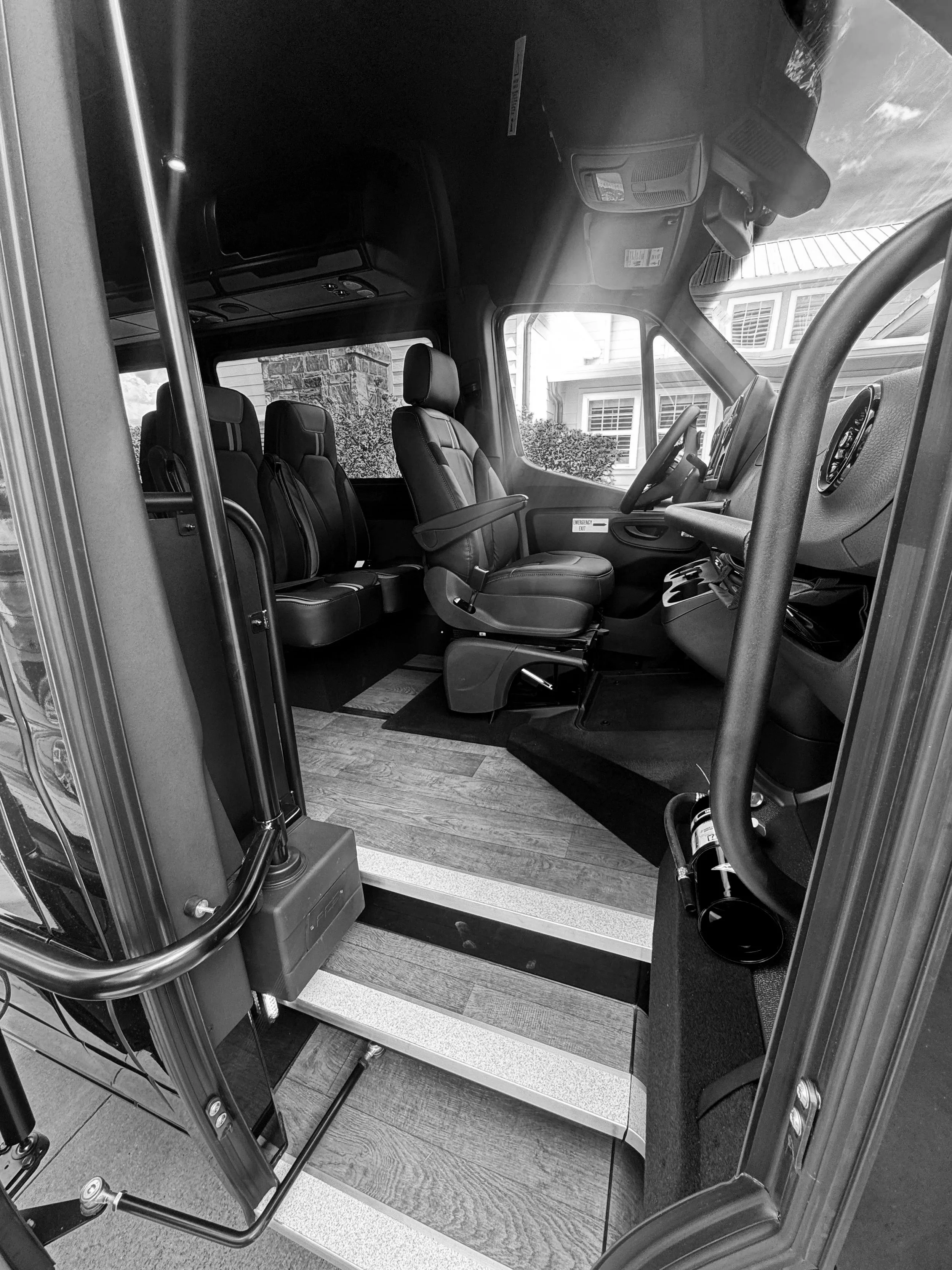 View of the interior of an emergency vehicle with multiple seats, dashboard, and control panels, with a residential house visible through the window.