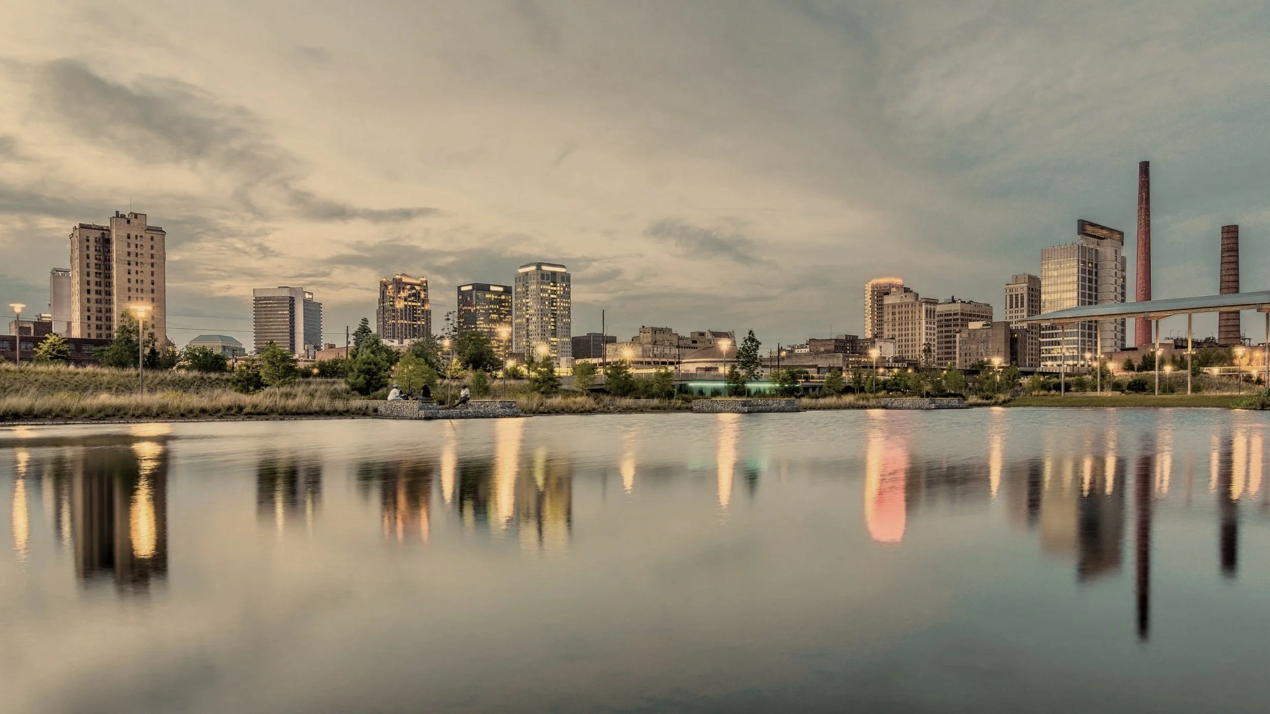 City skyline at dusk reflected in calm water with buildings and cloudy sky