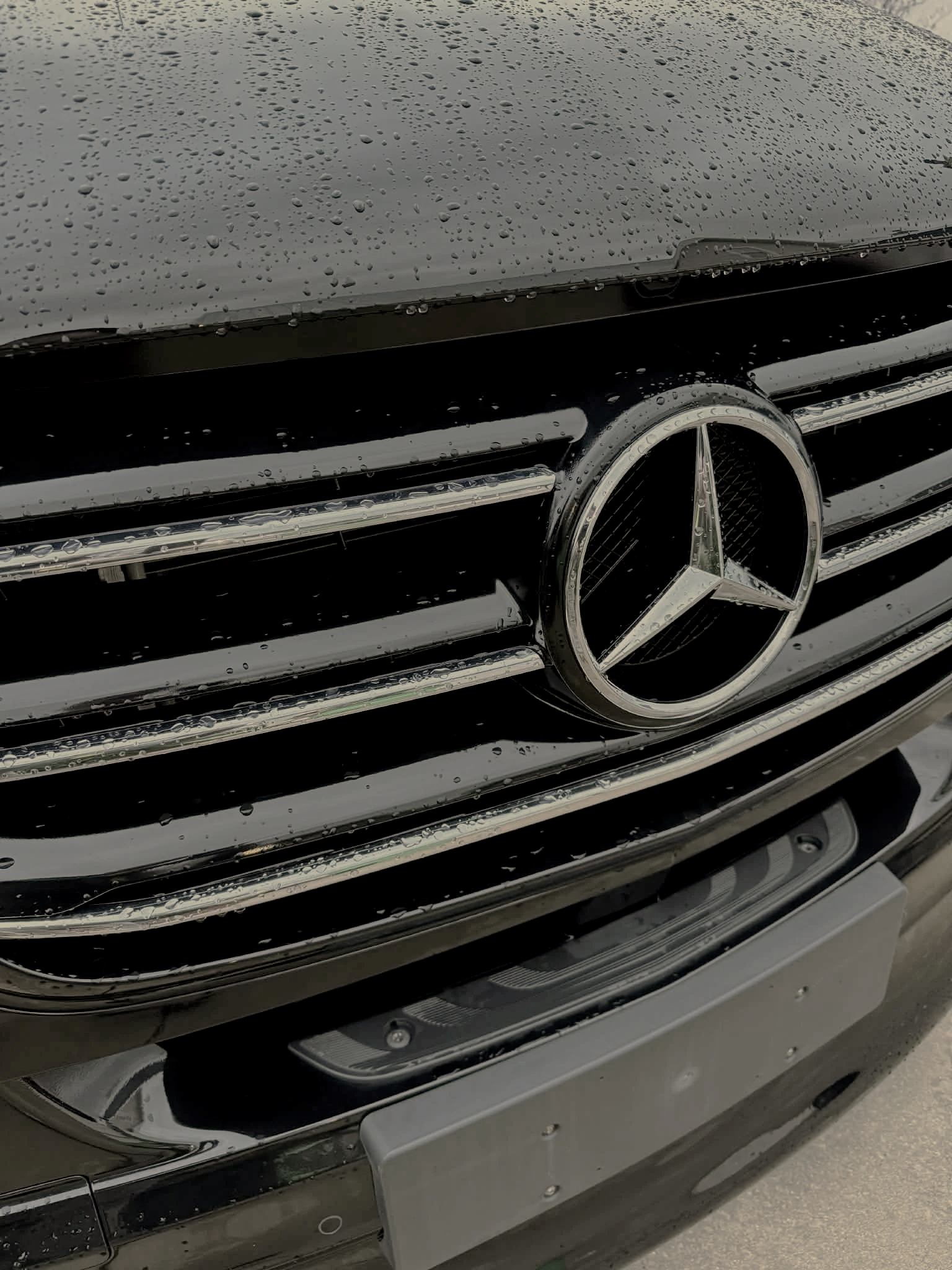 Close-up of the front grille of a black Mercedes-Benz vehicle with raindrops on its surface.