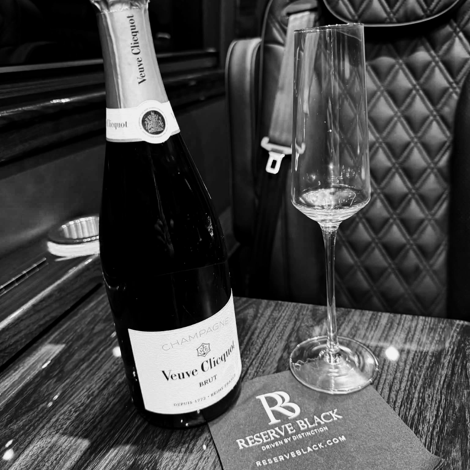 A bottle of Veuve Clicquot champagne and an empty champagne flute on a wooden table at a restaurant or bar.