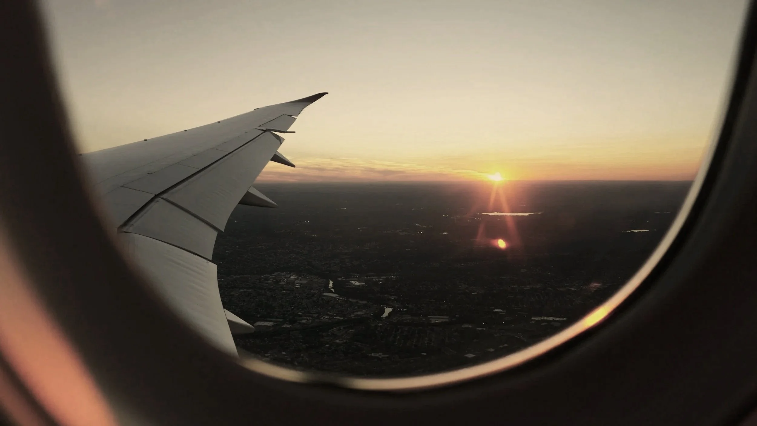 View of an airplane wing and sunset through an airplane window.
