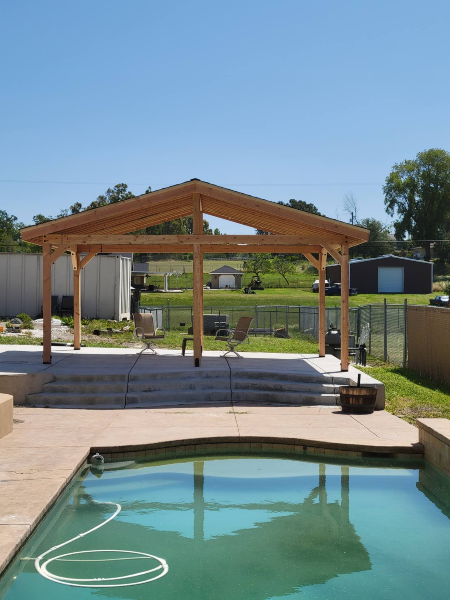Backyard with a pool and an unfinished wooden pergola on a sunny day.