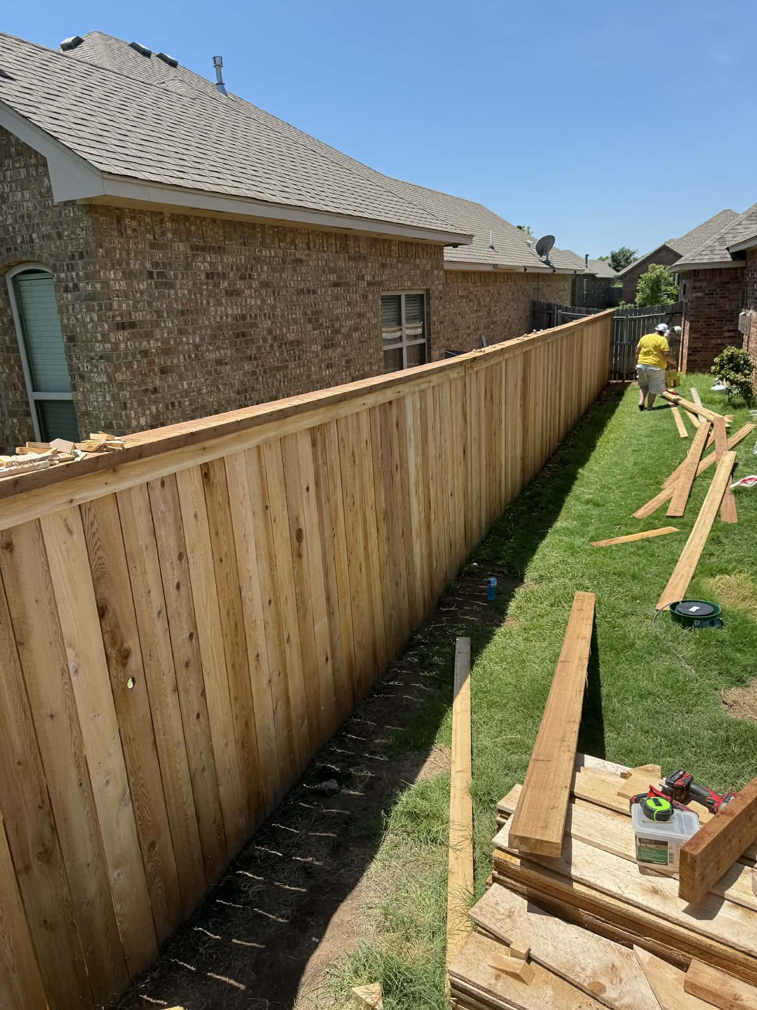Construction workers installing a wooden fence between two residential houses on a sunny day.