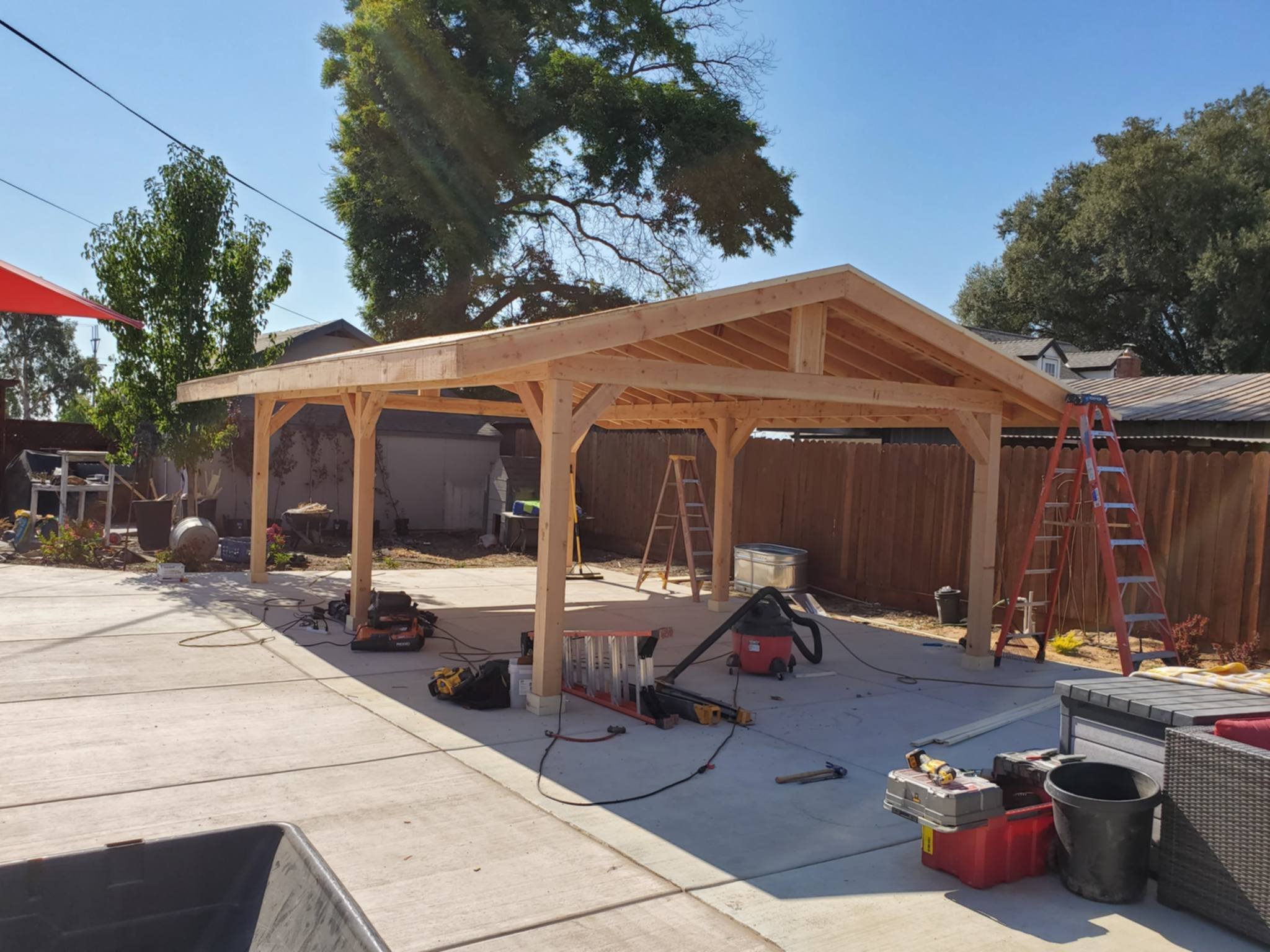 Wooden carport under construction in a backyard with tools and ladders
