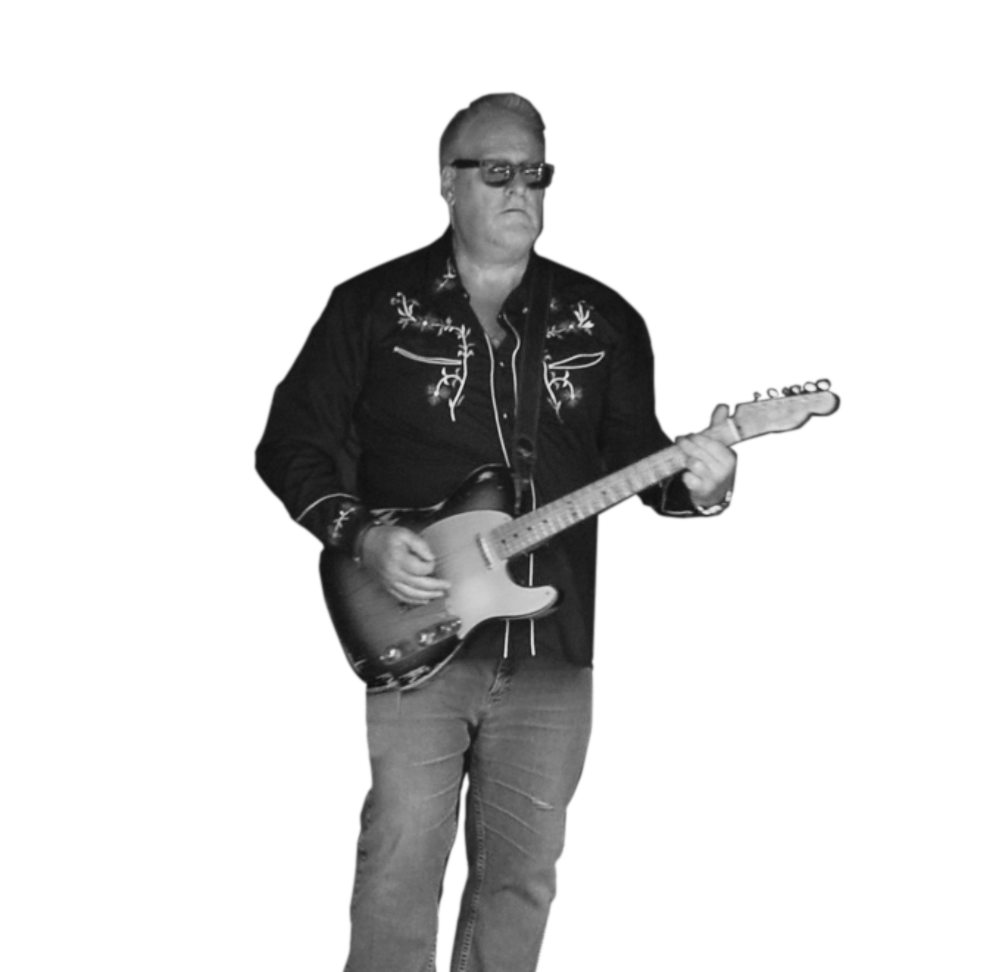A person standing and playing an electric guitar, wearing glasses, a dark embroidered shirt, and jeans, against a black background.