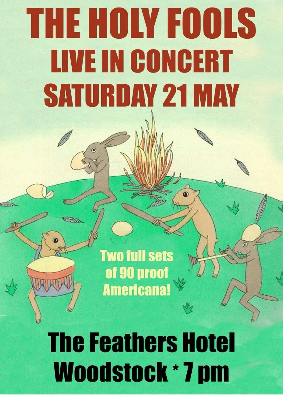 A cartoon concert poster for The Holy Fools, featuring rabbits and a hamster playing instruments around a campfire. The event is Saturday, May 21, at The Feathers Hotel in Woodstock at 7 pm.