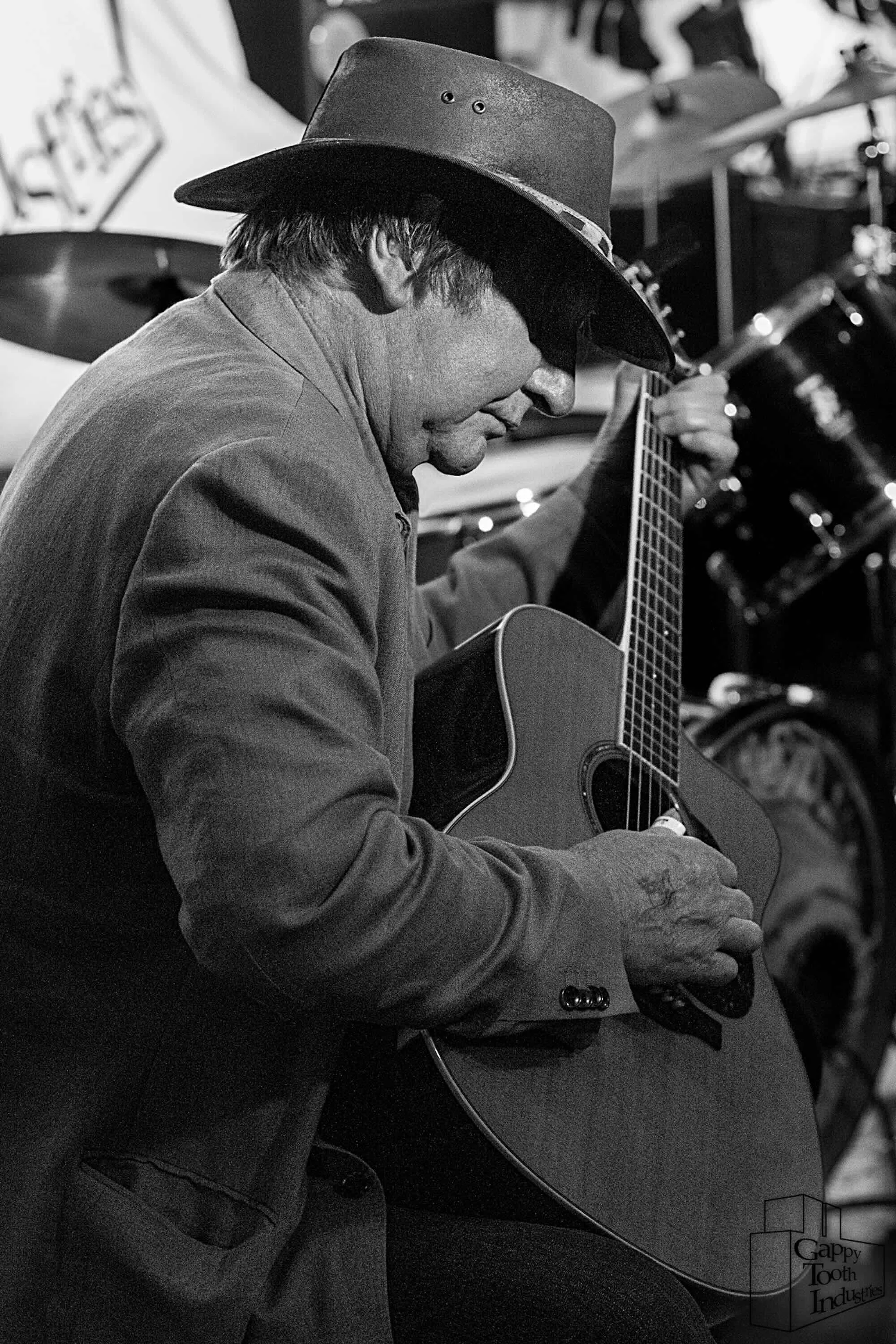 A man wearing a cowboy hat and a jacket playing an acoustic guitar.