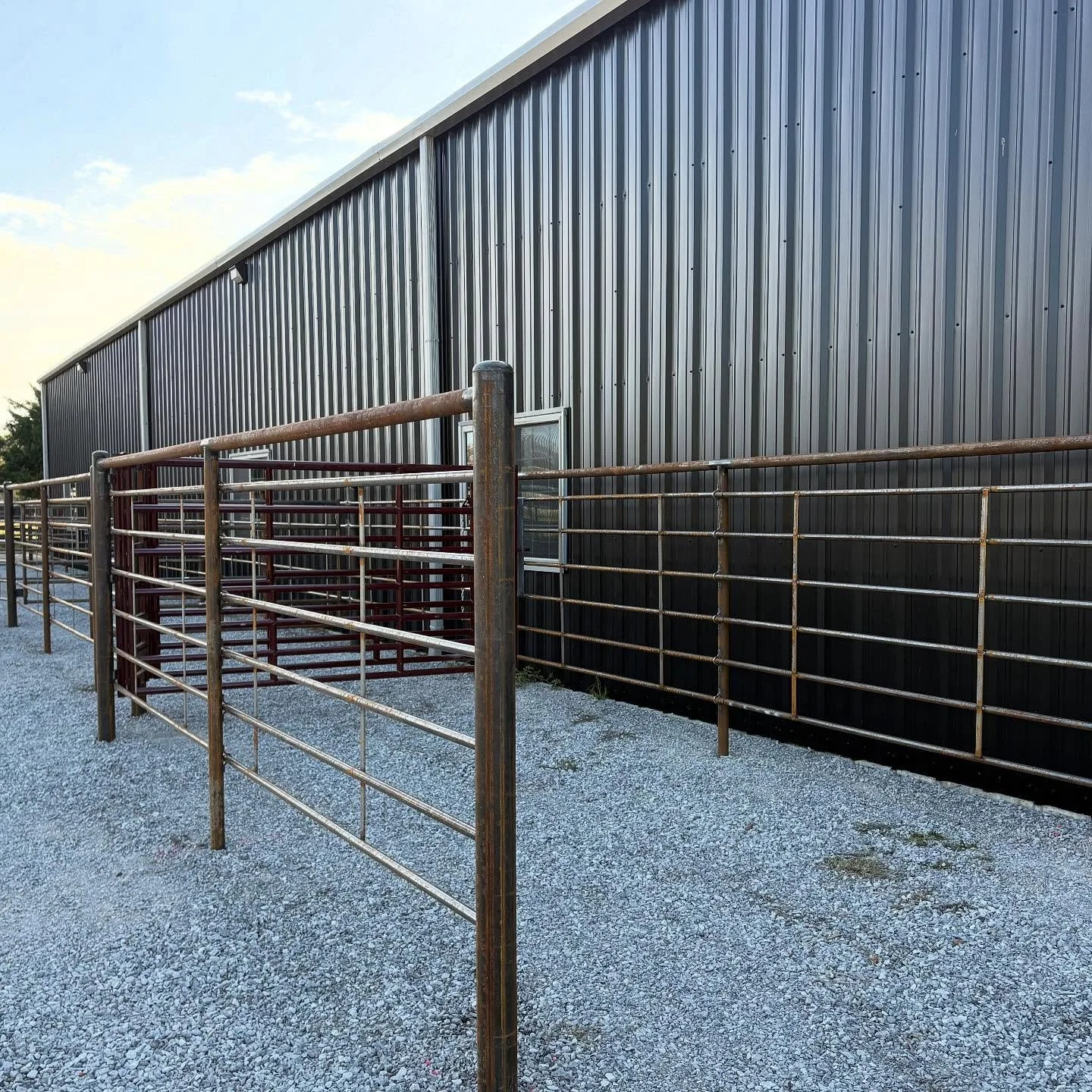 Outdoor scene with a black metal building, metal fencing, and gravel ground.
