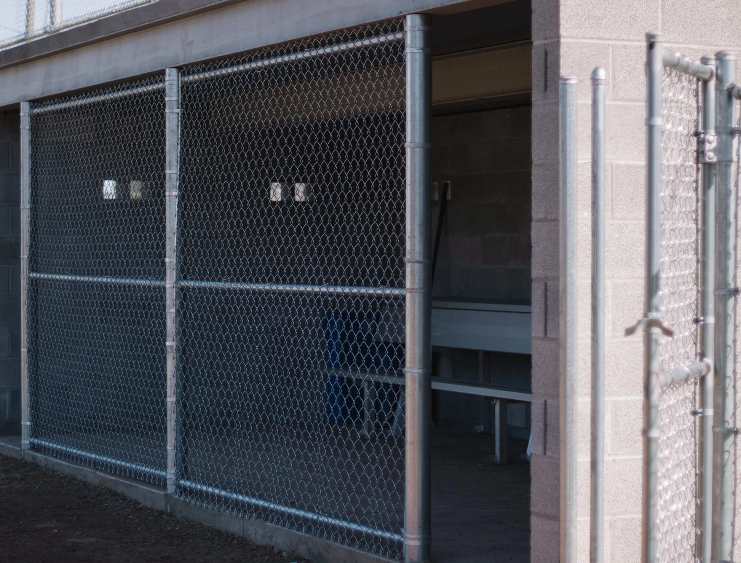 Metal chain-link fence around a structure with a small opening, concrete wall, and bench inside.