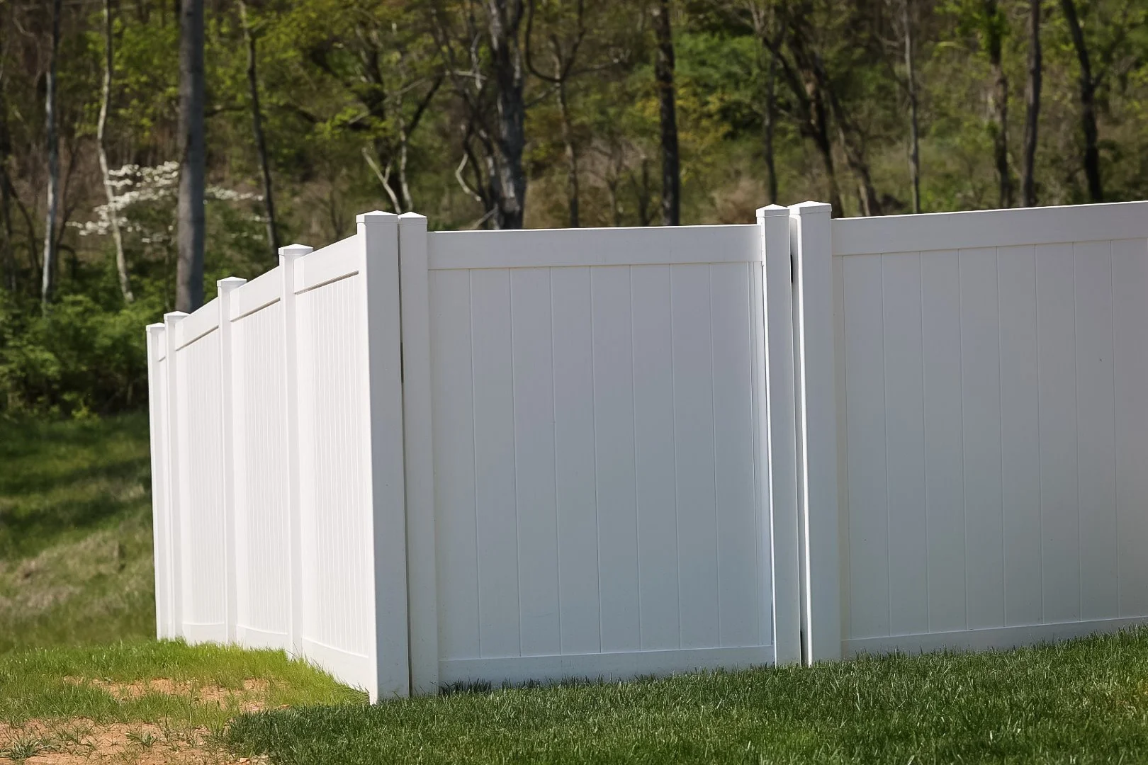 A white vinyl privacy fence on a grassy yard with trees in the background.