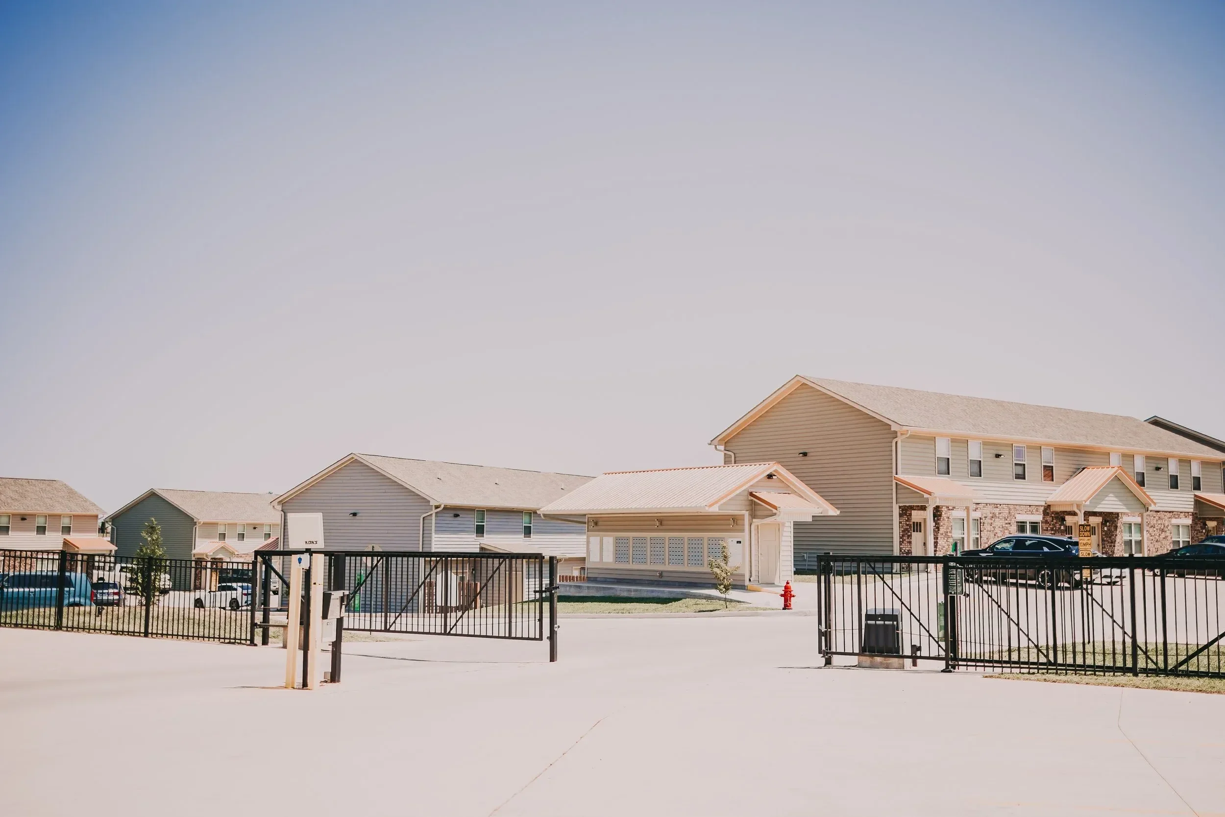 A gated residential community with houses, parked cars, and a small building in the center under a clear sky.