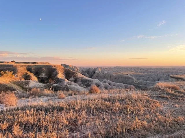 Sunset over a dry, hilly landscape with sparse vegetation and a clear sky.