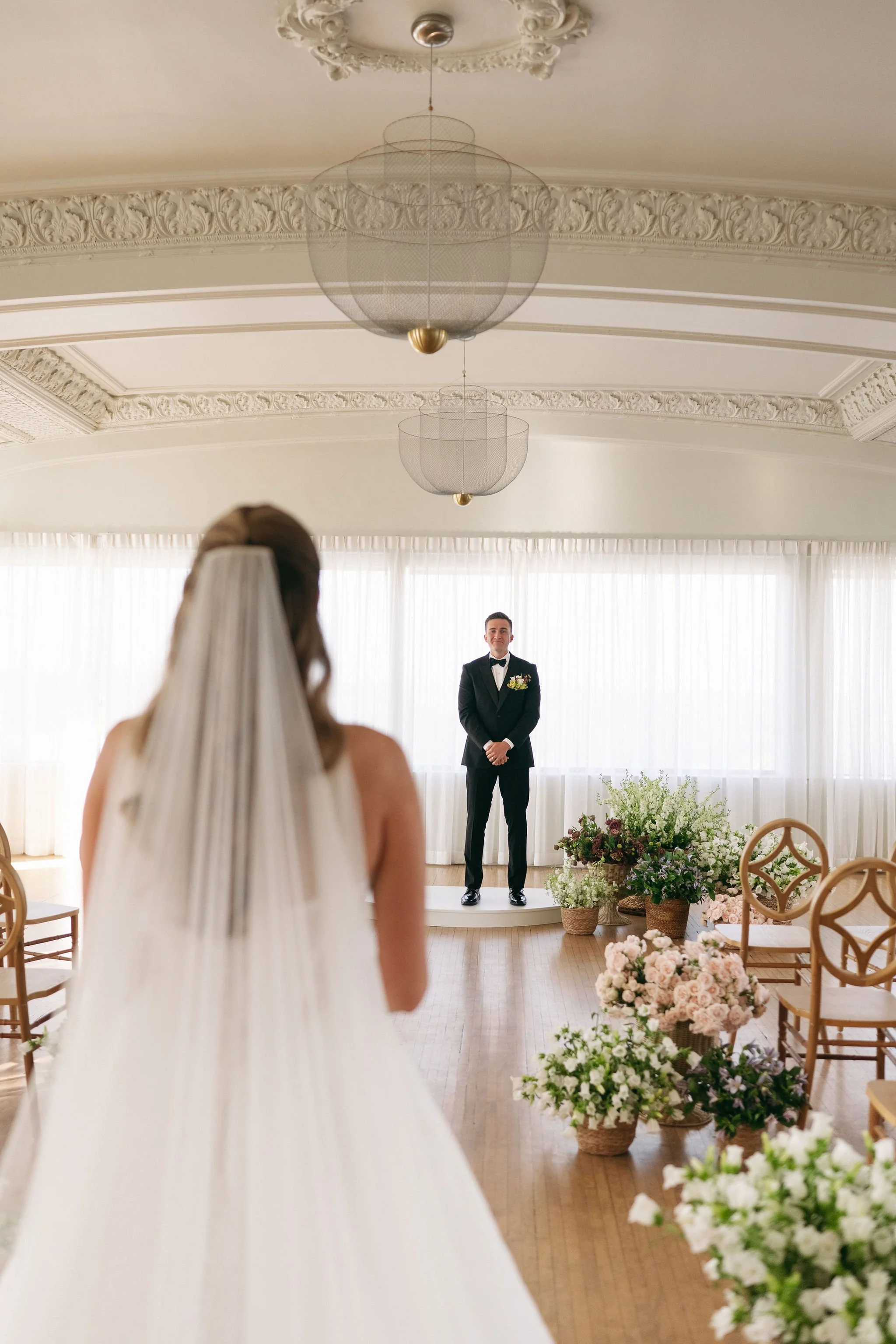 Bride facing groom standing on a small platform in a decorated indoor venue for a wedding ceremony.