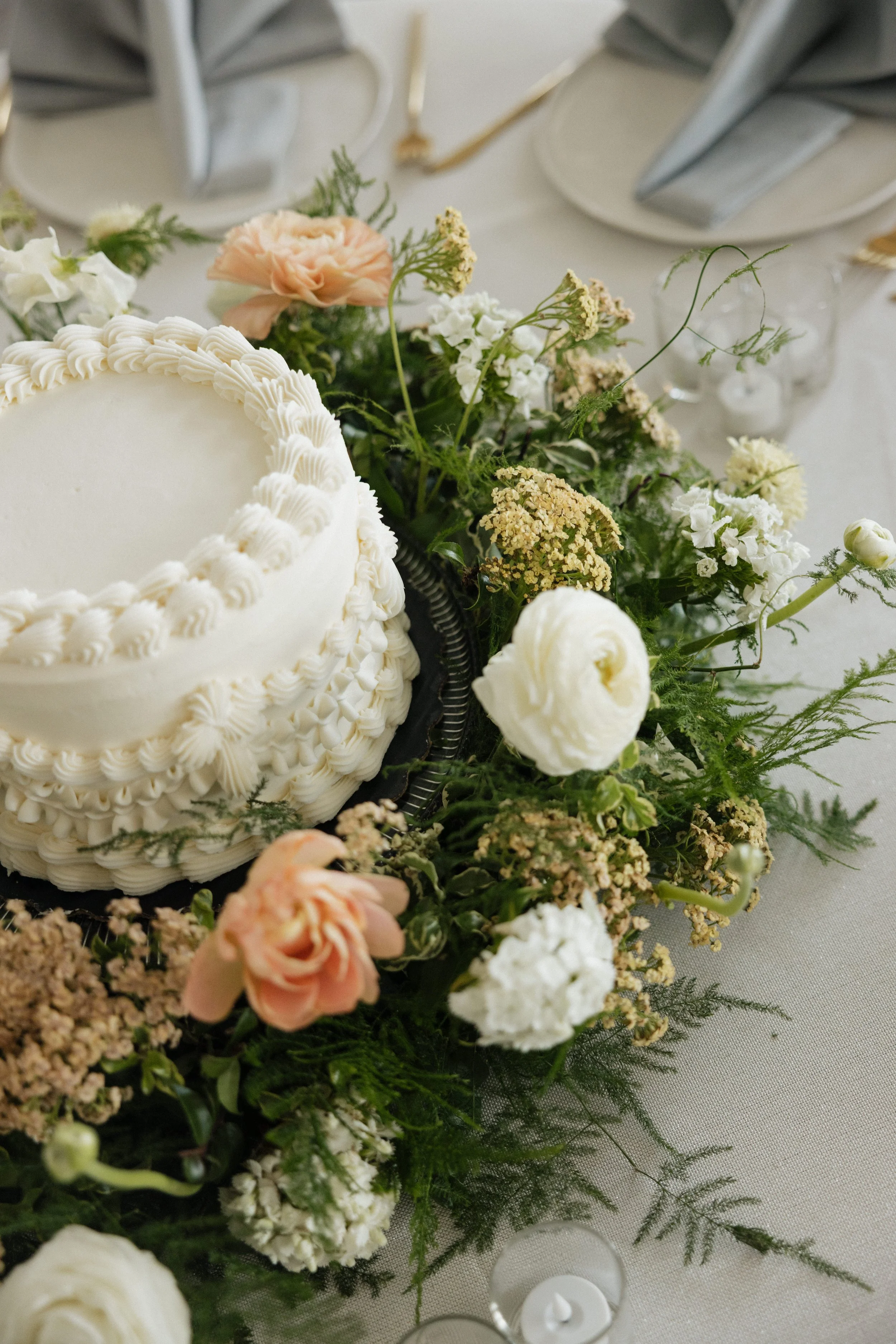 Decorated wedding cake on a table surrounded by flowers and greenery.