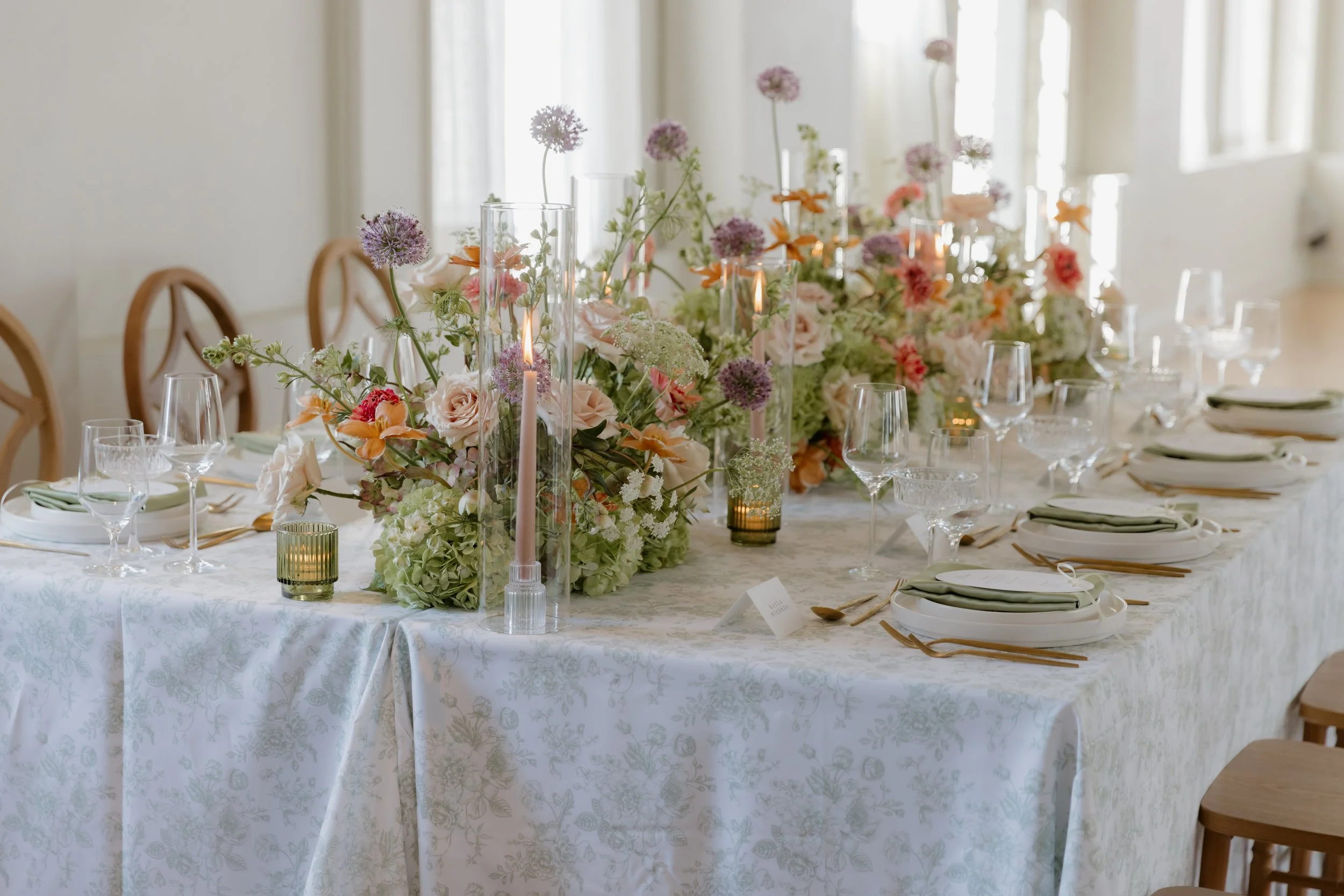 Elegant banquet table setup with floral centerpiece, candles, wine glasses, and place settings at a well-lit dining event.