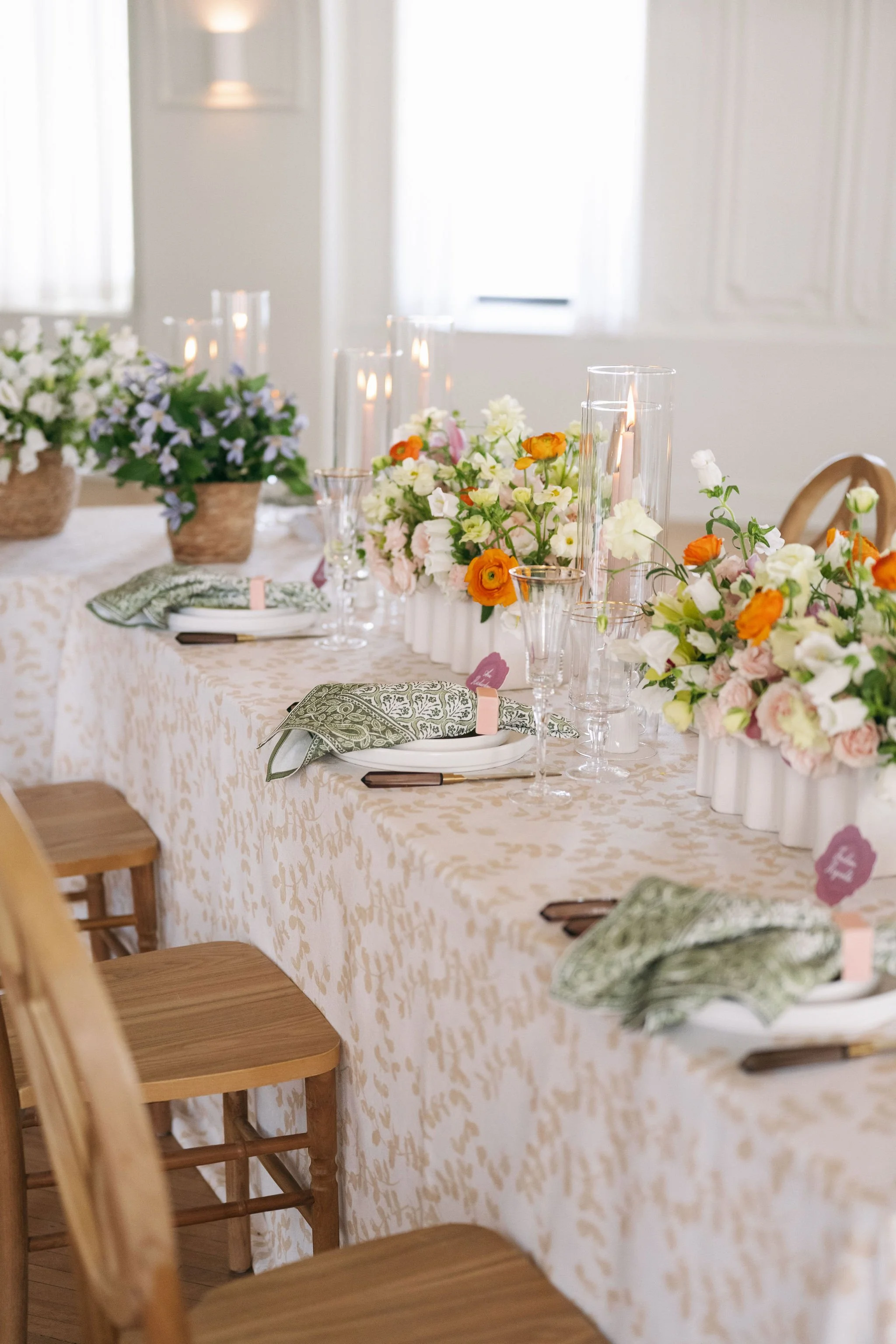 A decorated banquet table with floral centerpieces, candles, glasses, and place settings with green patterned napkins in an elegant room.
