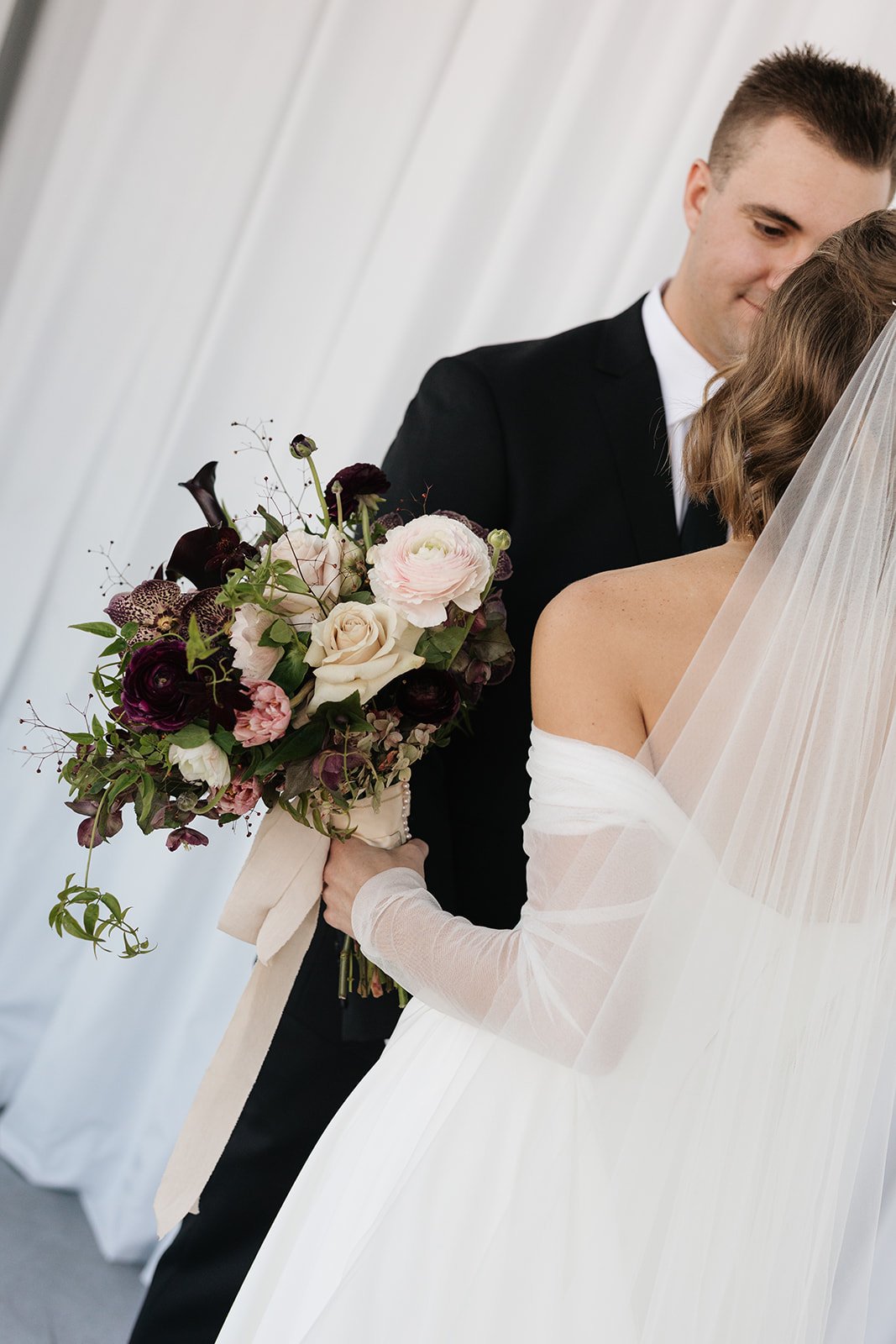 Bride holding a bouquet of flowers facing groom during wedding ceremony.