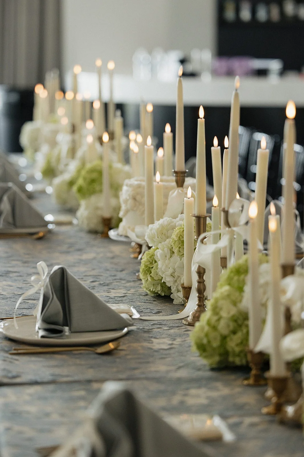 A long dinner table decorated with white flowers, tall white candles, and elegant place settings for a formal event.