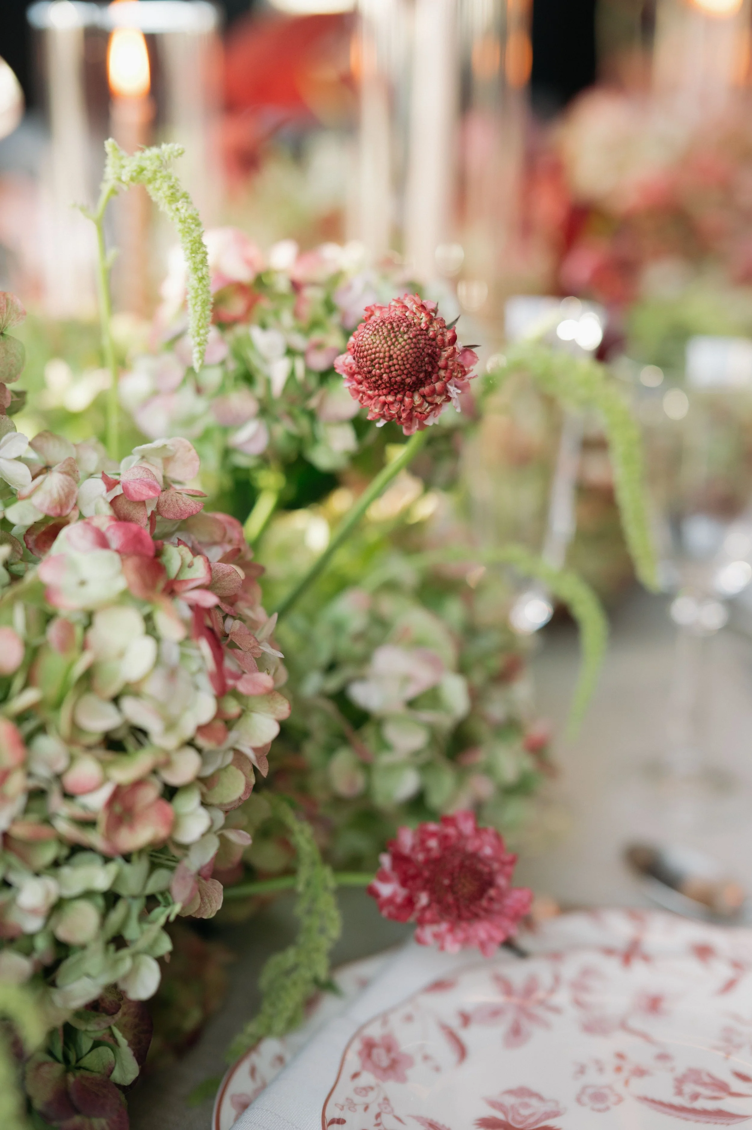 Close-up of a floral centerpiece featuring pink and green hydrangeas and red flowers with a blurred background.