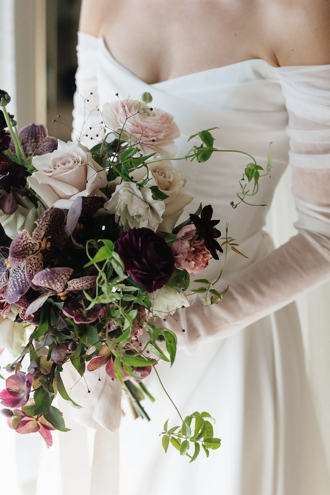 Part of a woman in a white wedding dress holding a bouquet of pink, white, purple, and green flowers.