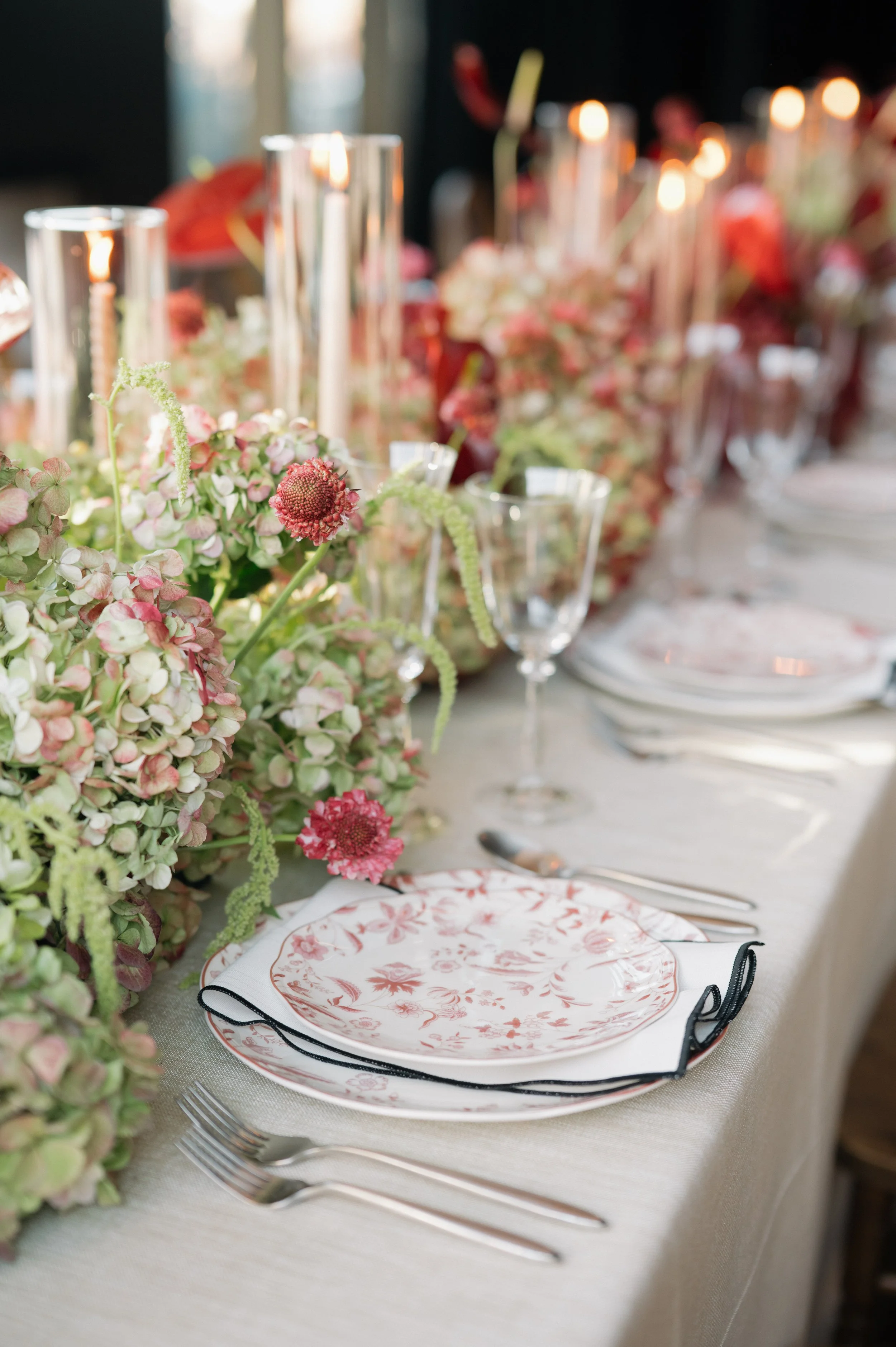 Elegant dining table with floral centerpiece, floral-patterned plates, glassware, and silverware for a formal event.