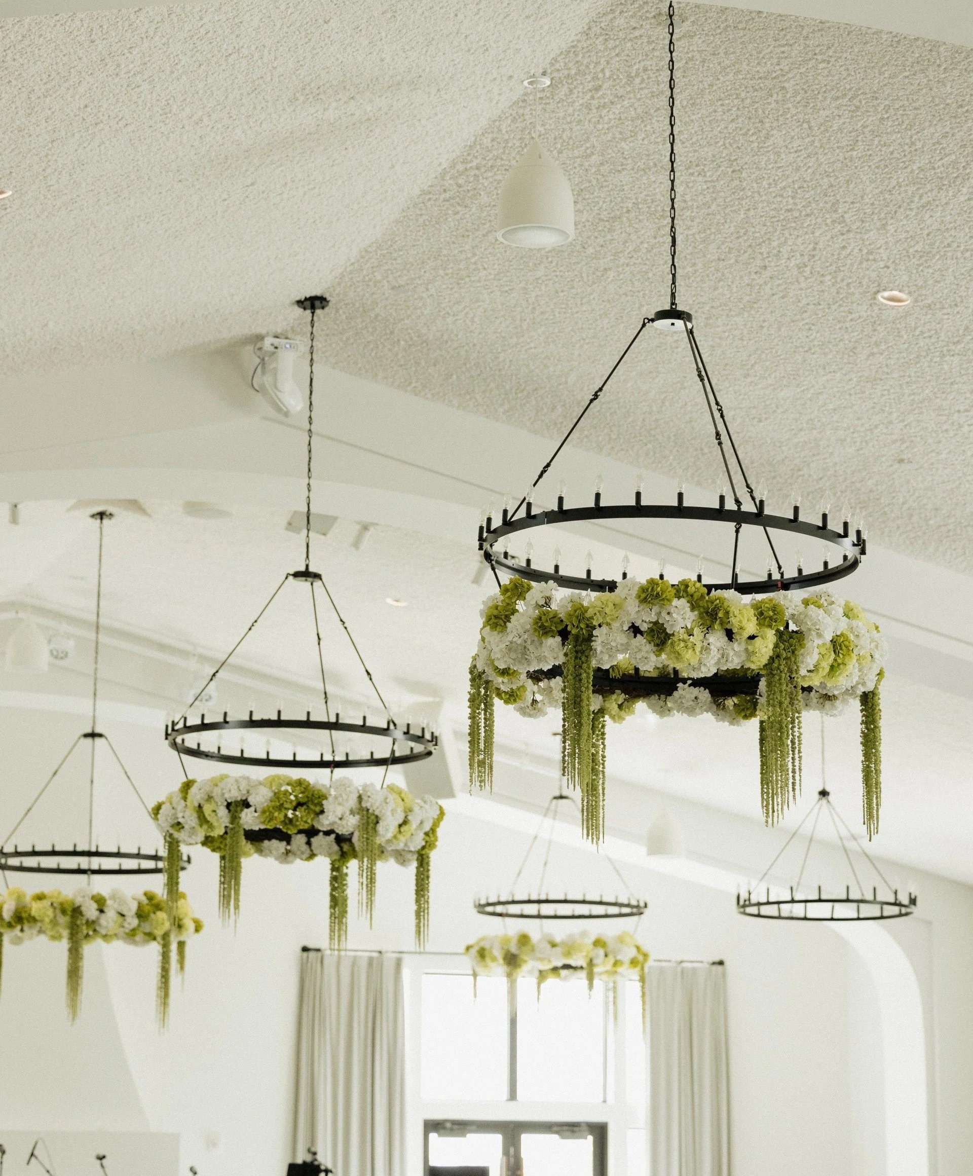 Indoor venue with floral chandeliers hanging from the ceiling, decorated with white and green flowers and greenery.