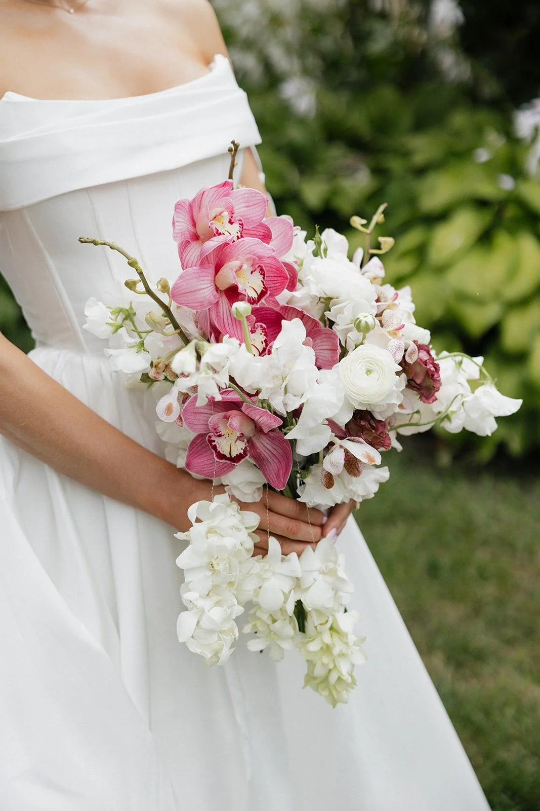 A woman in a white dress holding a bouquet of pink, white, and purple flowers outside