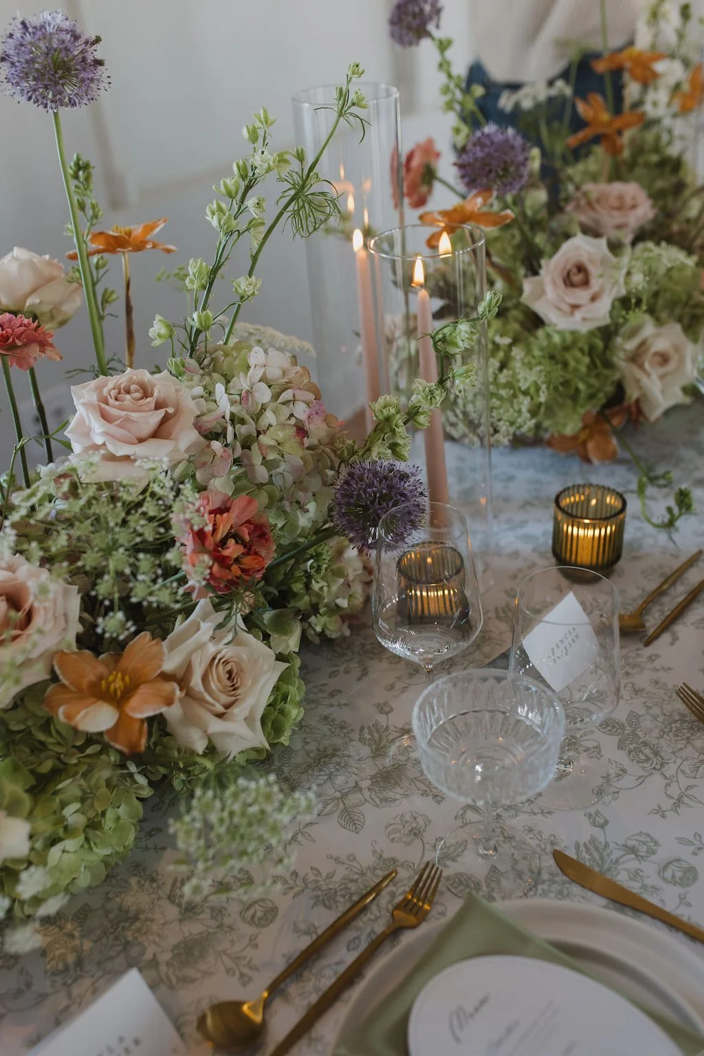 Elegant table setting with floral centerpiece, candles, wine glasses, and gold utensils