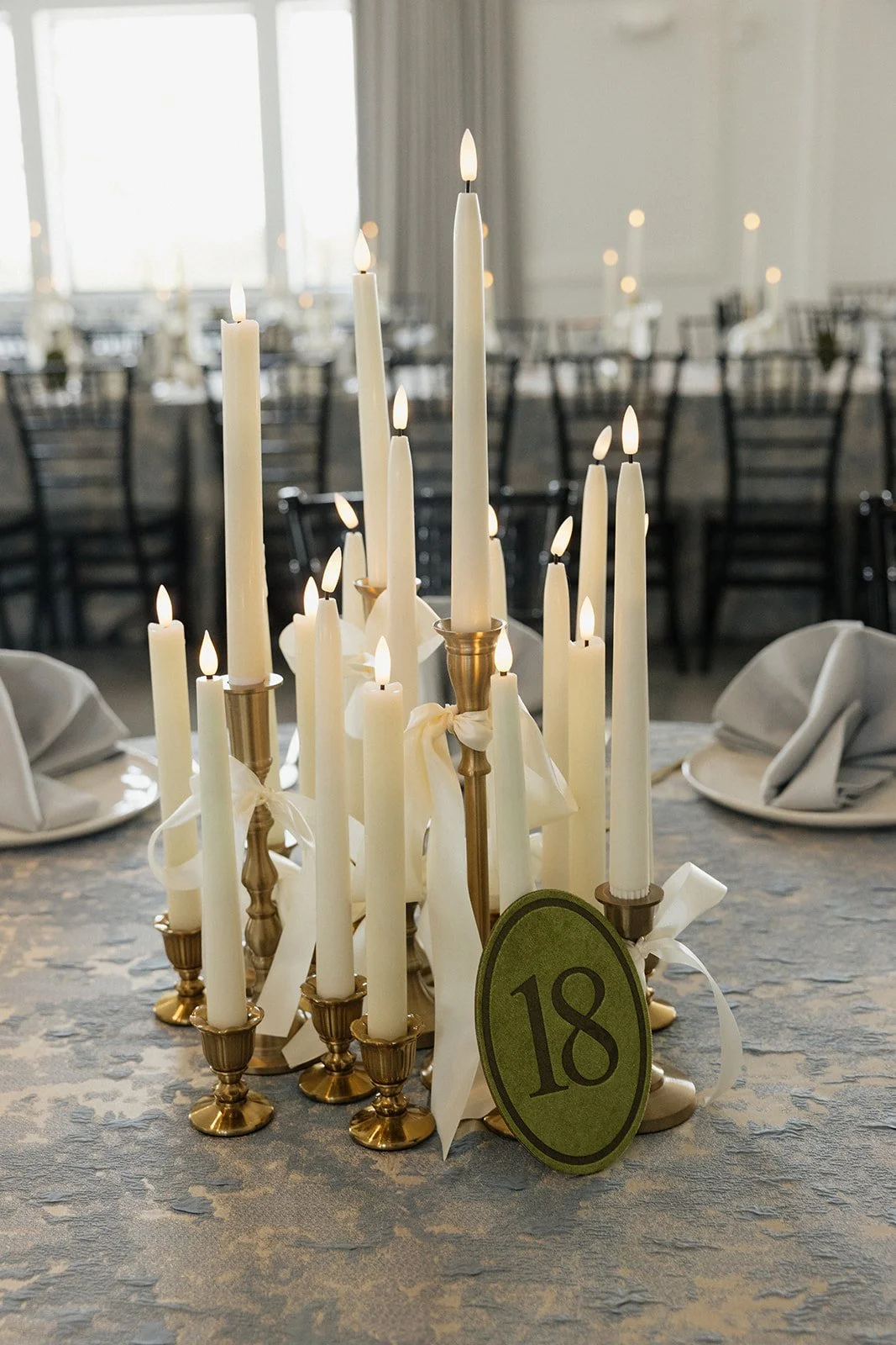 Table centerpiece with white candles and a green card with the number 18 at an elegant event venue.