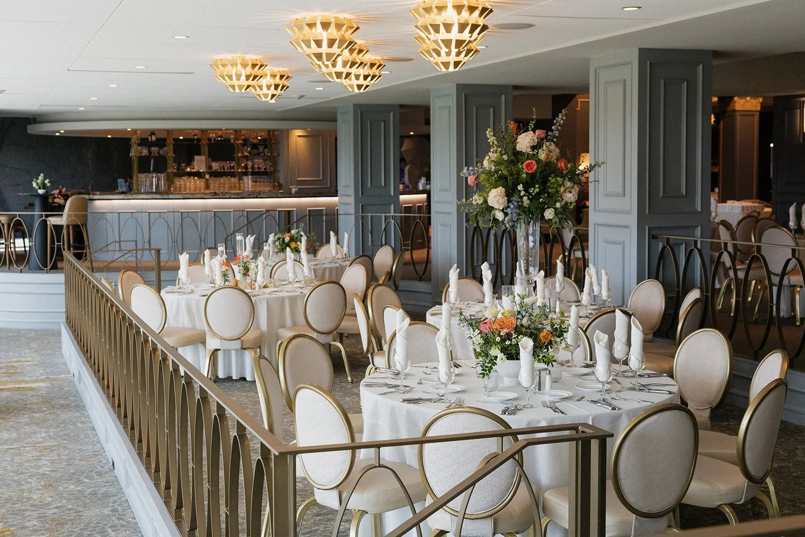 Elegant dining setup for a special event with round tables decorated with floral arrangements and white napkins in a sophisticated restaurant or banquet hall.