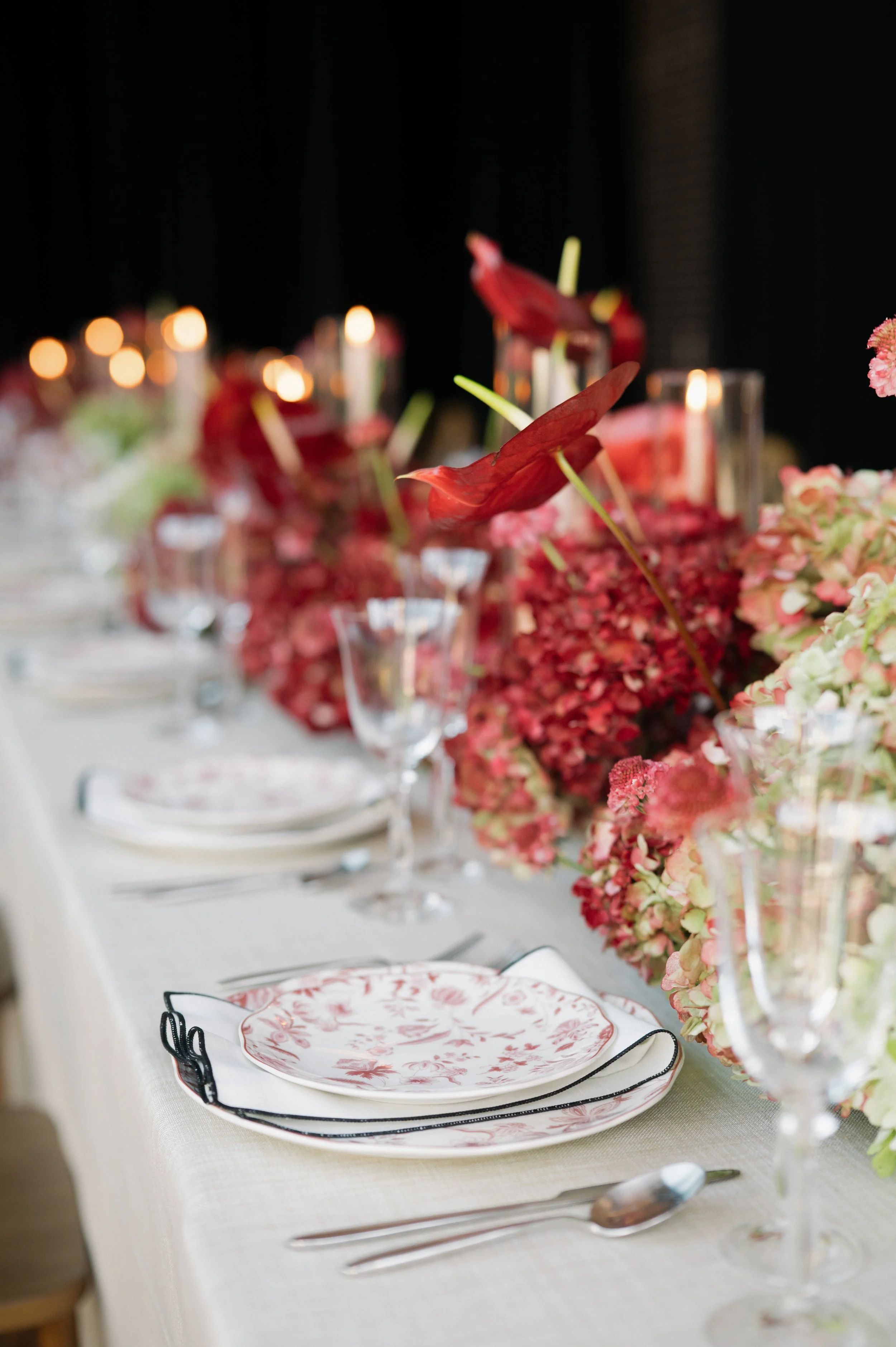 Elegant dining table decorated with pink and red flowers, candles, and glassware for a formal event.