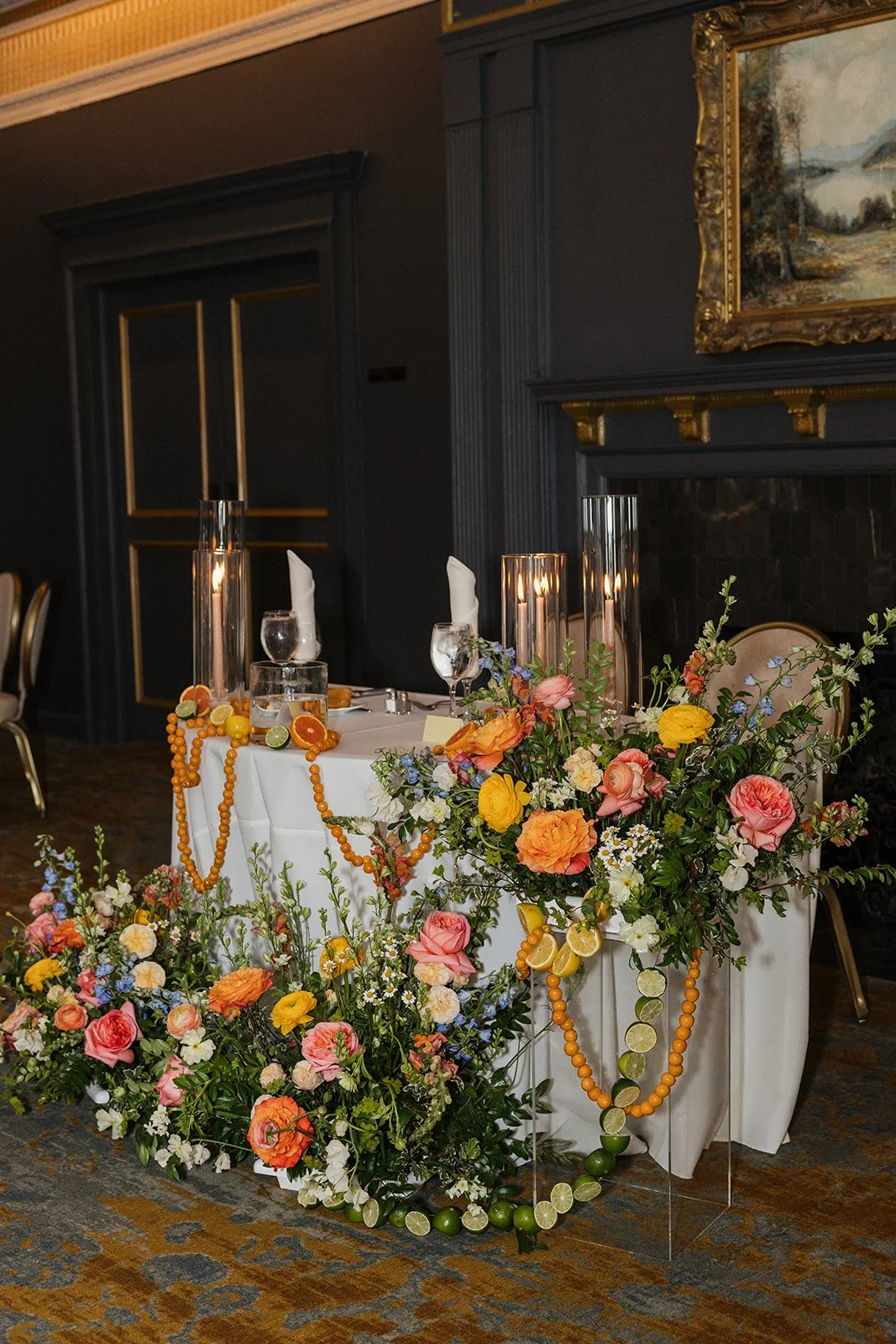 Decorated banquet table with colorful floral arrangements, orange beads, and citrus fruit slices at a formal event
